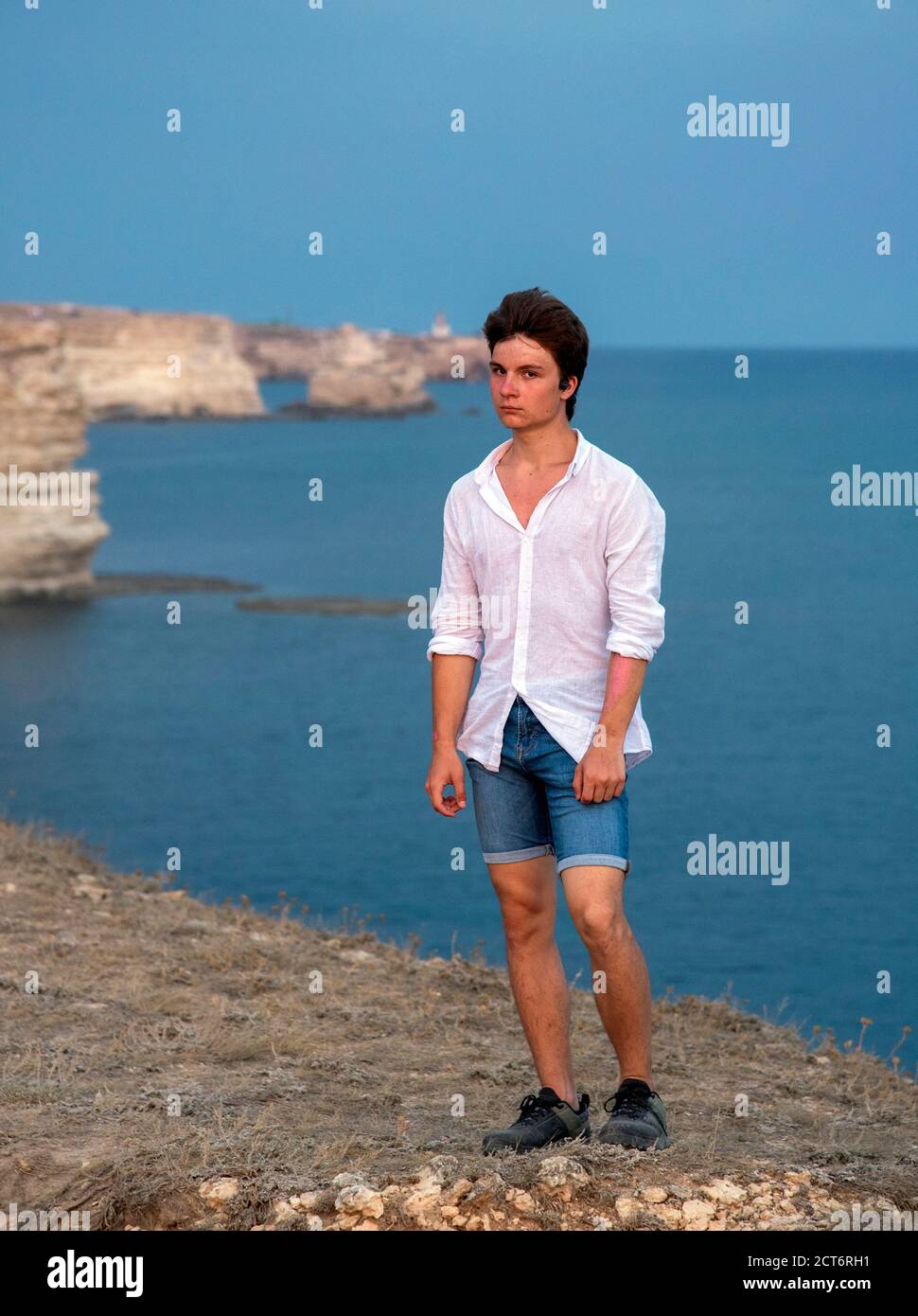Un giovane si erge su una spiaggia rocciosa al tramonto. Foto Stock