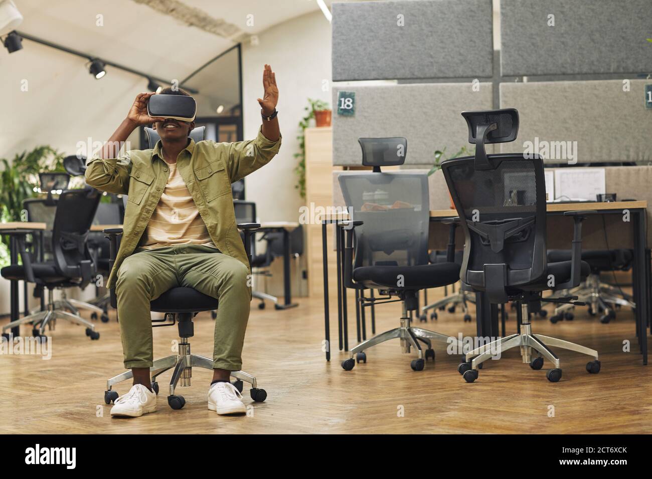 Ritratto a tutta lunghezza di un giovane afroamericano che indossa outfit VR in ufficio e che ti immergi nella realtà, copia spazio Foto Stock