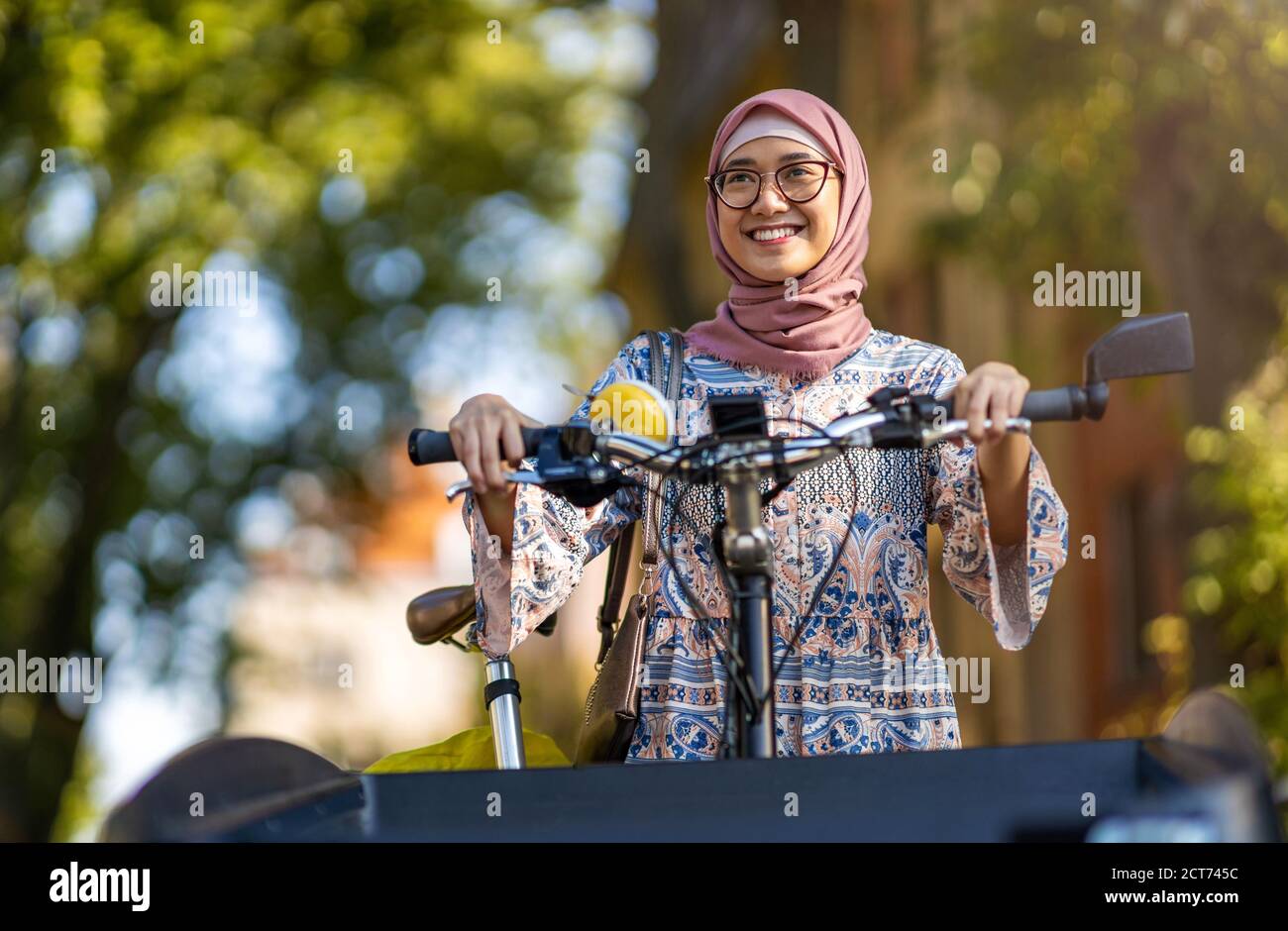 Donna musulmana sicura che usa la bicicletta da carico nell'area urbana Foto Stock