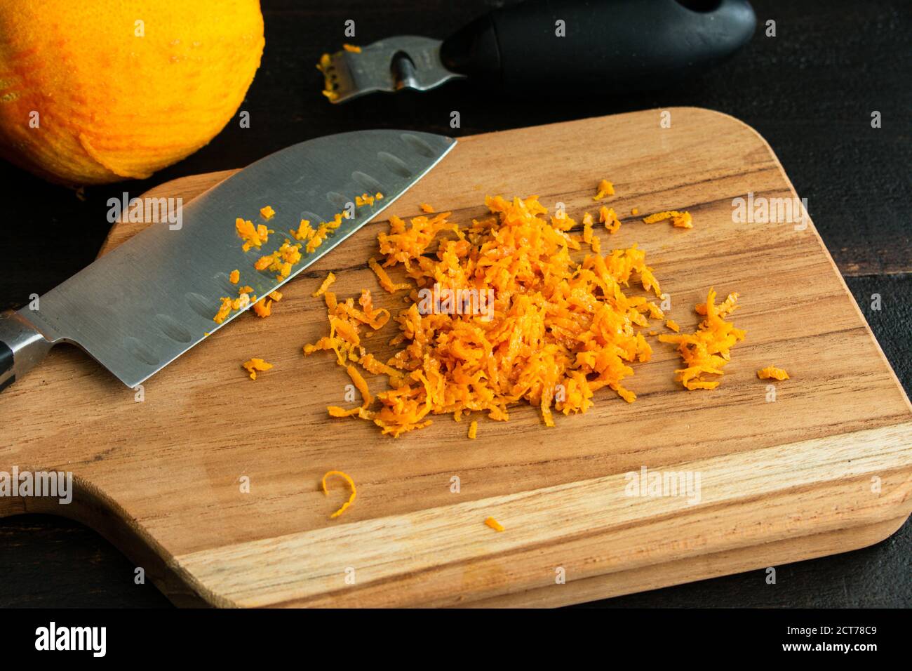 Zesting un arancione: Scorza arancione su un tagliere di legno Foto Stock
