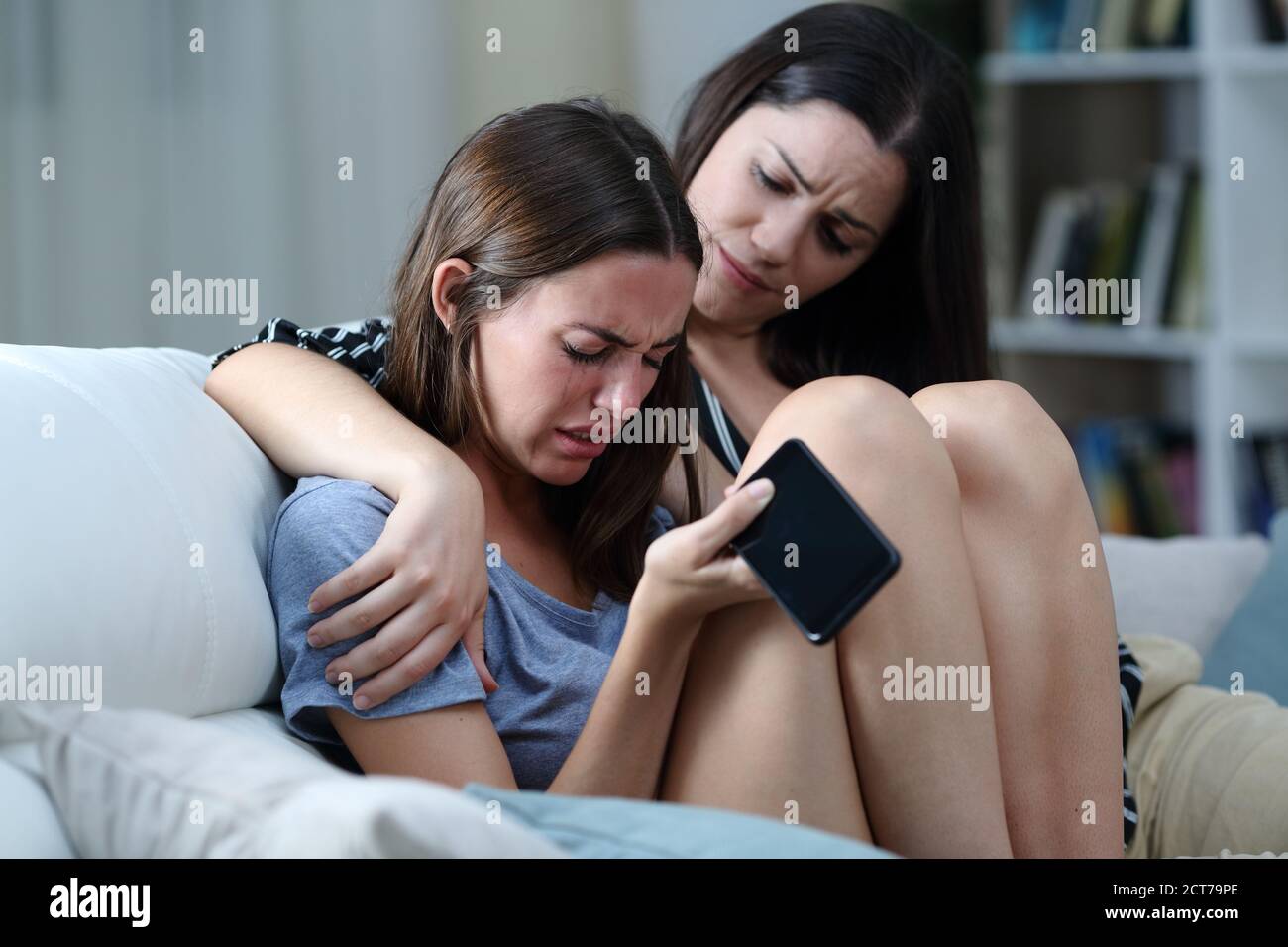 Triste teen con il telefono che è confortato da sua sorella sopra un divano nel soggiorno di casa Foto Stock