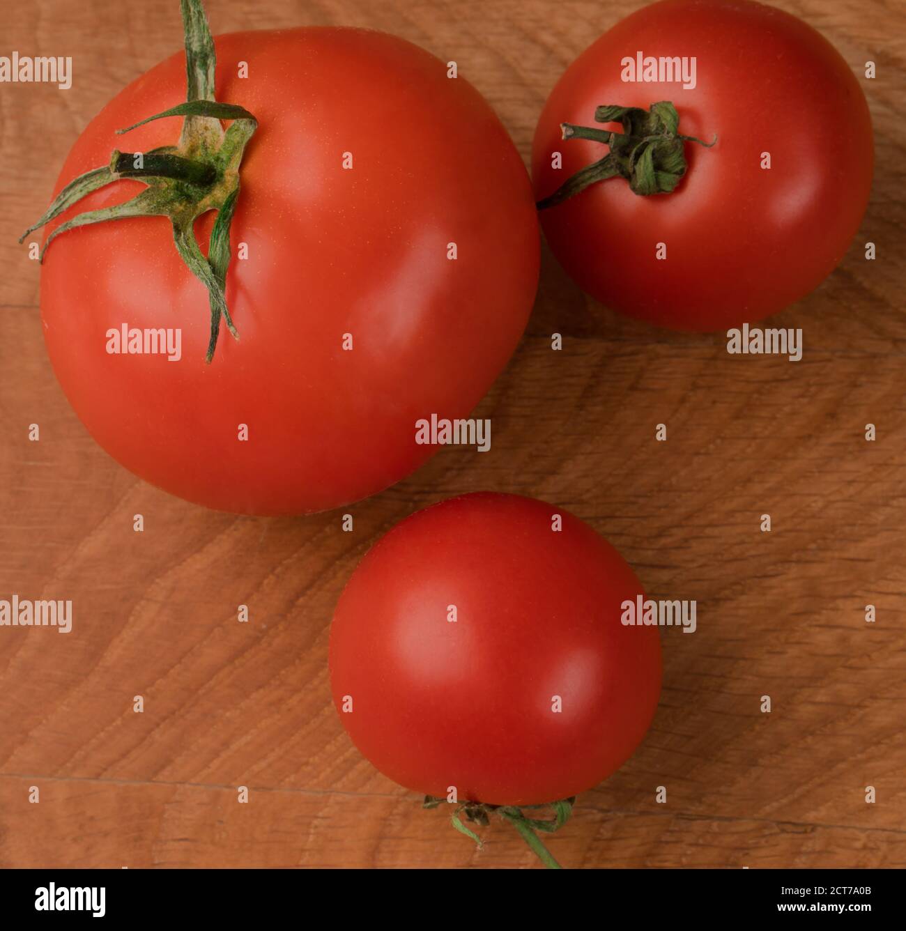 Tre pomodori rossi, uno in più e due più piccoli su una tavola di legno Foto Stock