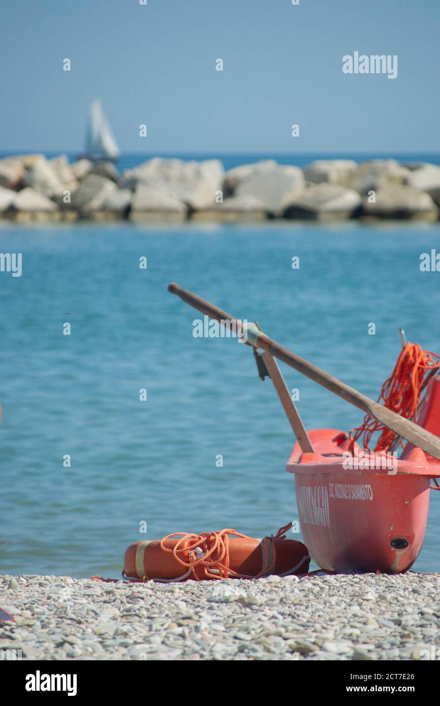 tipica barca a remi in legno color arancio con bagnini. Una barca a vela sullo sfondo Foto Stock
