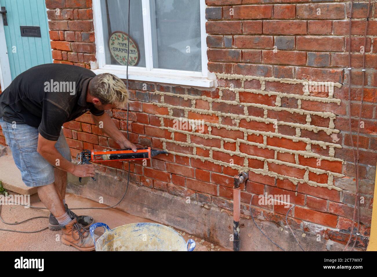 Uomo re-puntando/applicando mortaio ai giunti di mattone su un cottage a Lavenham, Suffolk, Regno Unito. Foto Stock