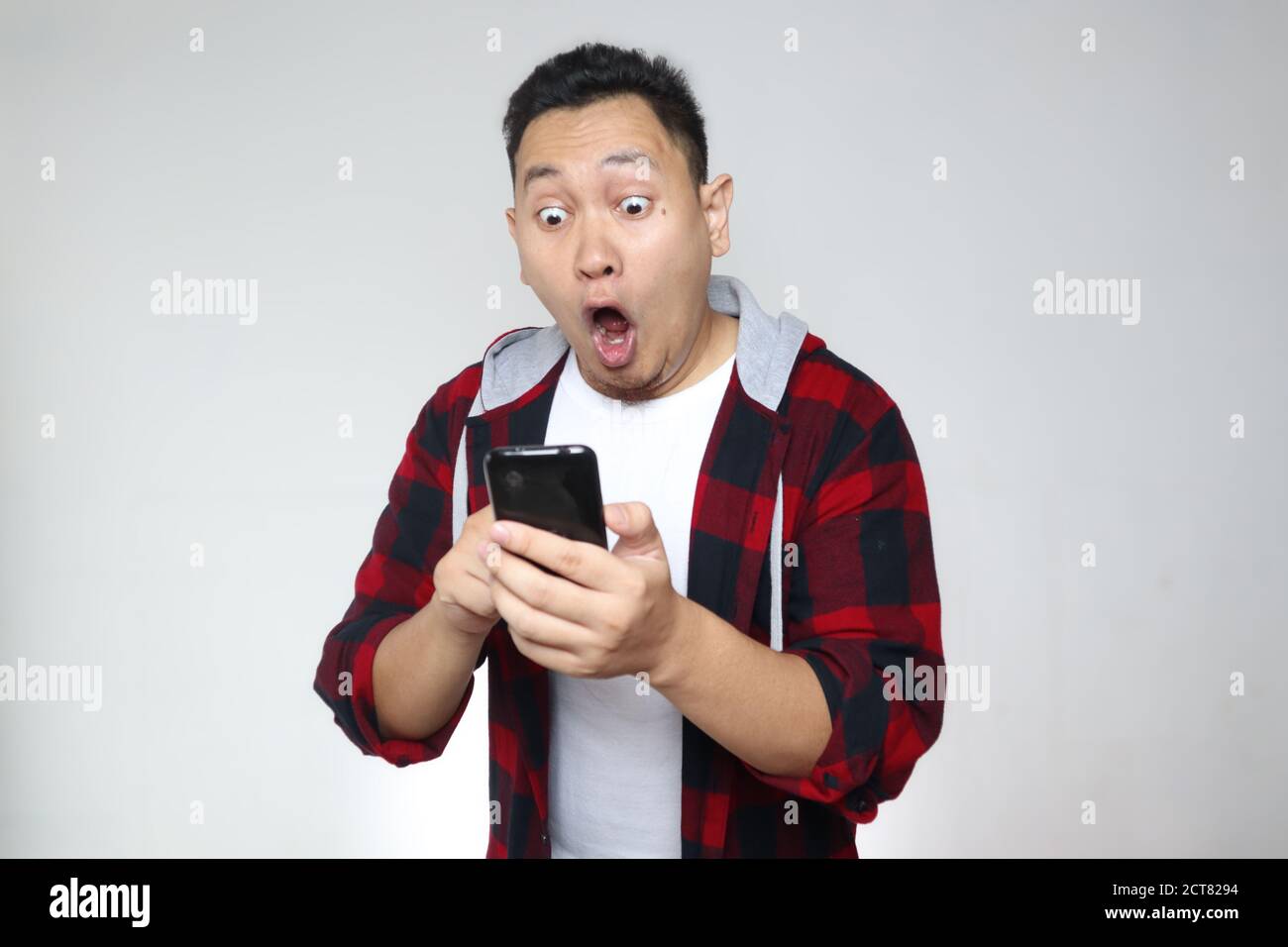 Attraente giovane asiatico che legge testando chattando sul suo telefono, scioccato sorpresa espressione Foto Stock