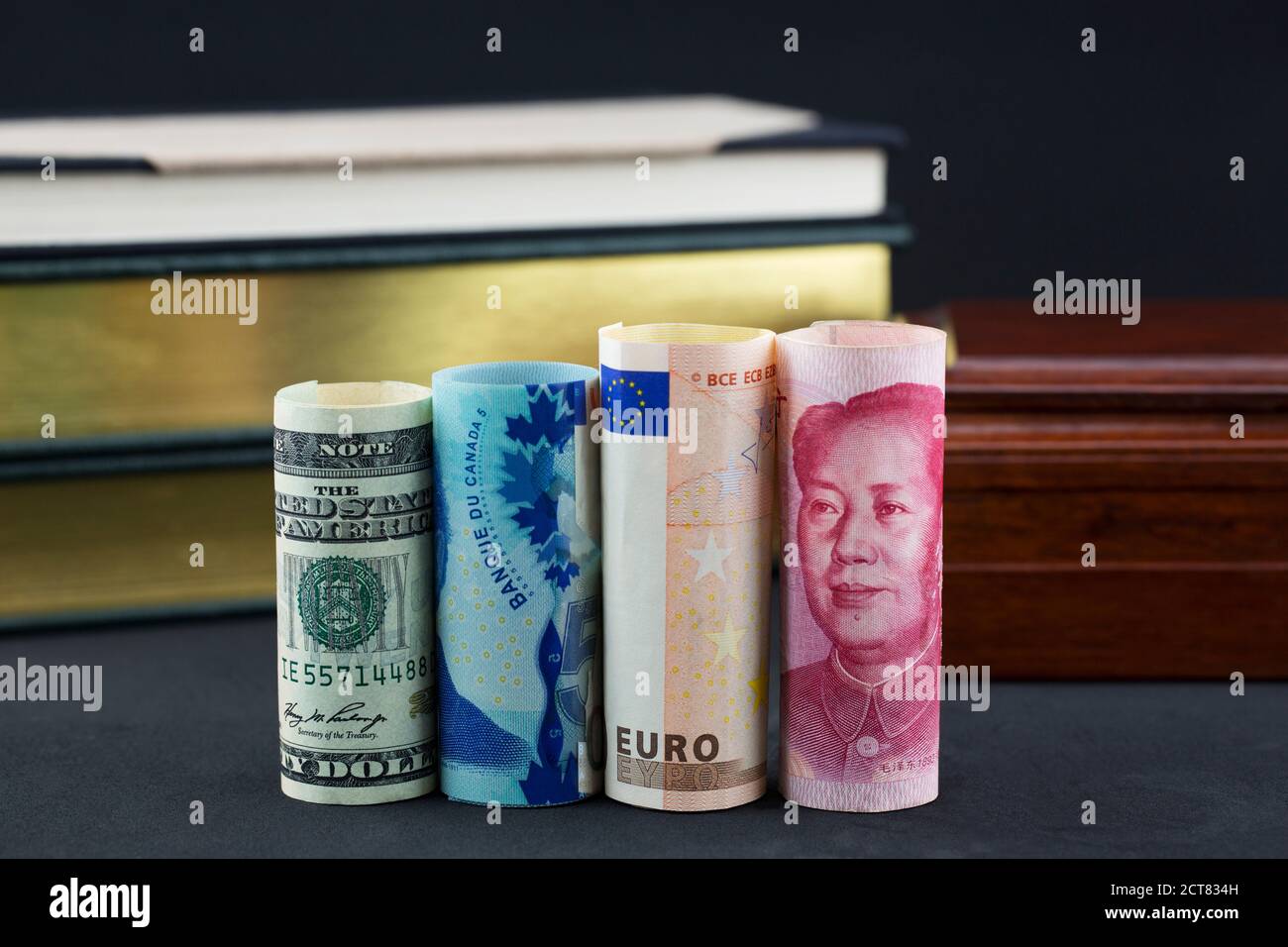 Collegamento delle finanze, delle strategie e delle economie di affari mondiali riflesso in quattro valute davanti ai libri e alla scatola di legno Foto Stock