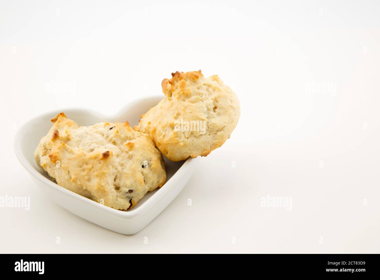 Biscotti caldi appena sfornati a goccia fatti con uvetta, noci e yogurt messi in piatto a forma di cuore su sfondo bianco Foto Stock