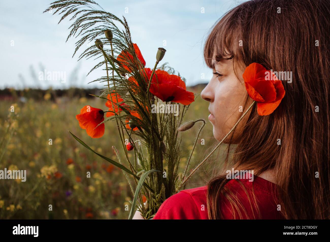 Un ritratto giovane bianco della ragazza teen in piedi profilo con la sua schiena alla macchina fotografica con rosso fiore papaveri fiori bouquet Foto Stock