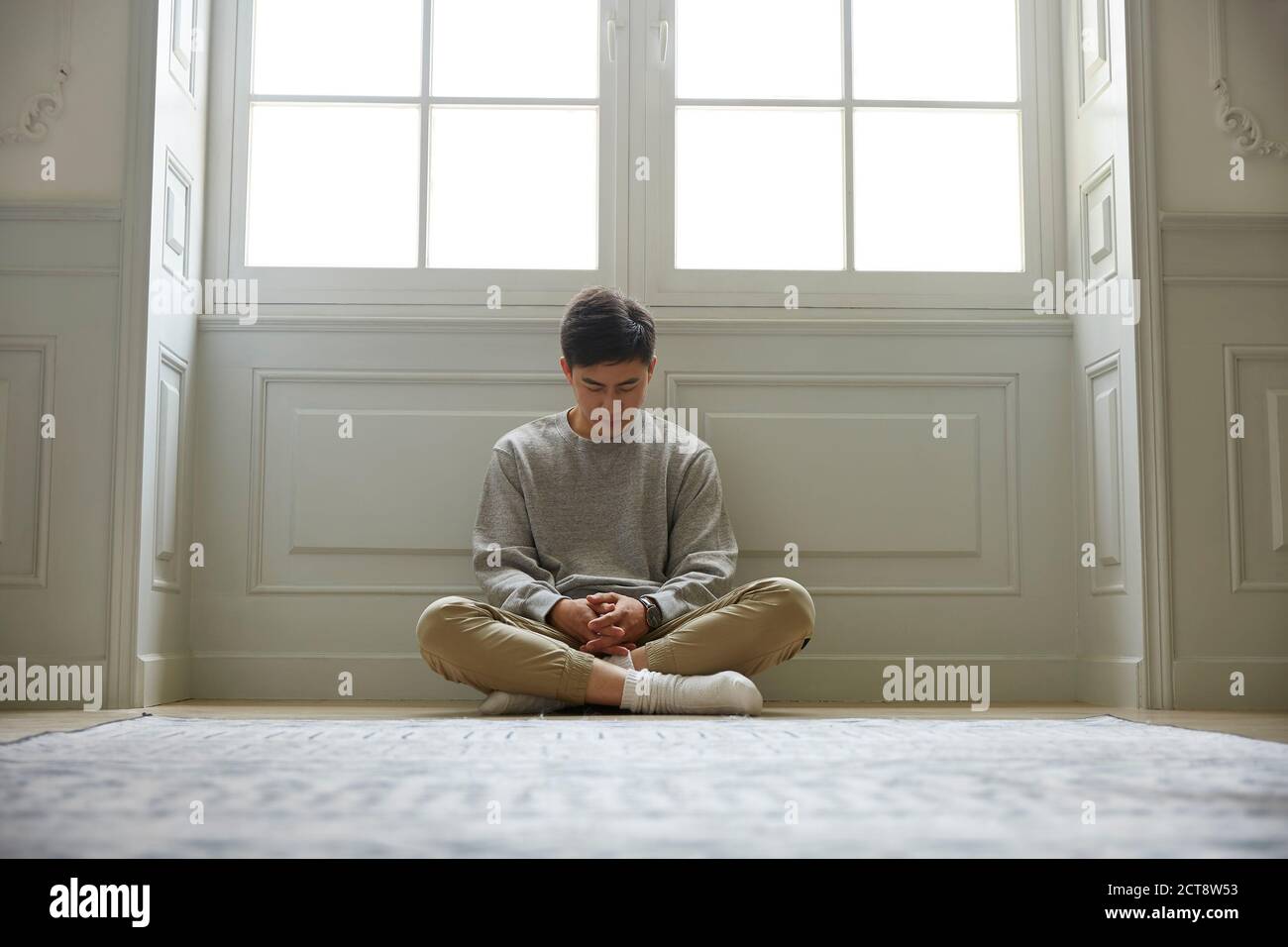 giovane asiatico seduto sul pavimento a casa testa giù gambe incrociate Foto Stock