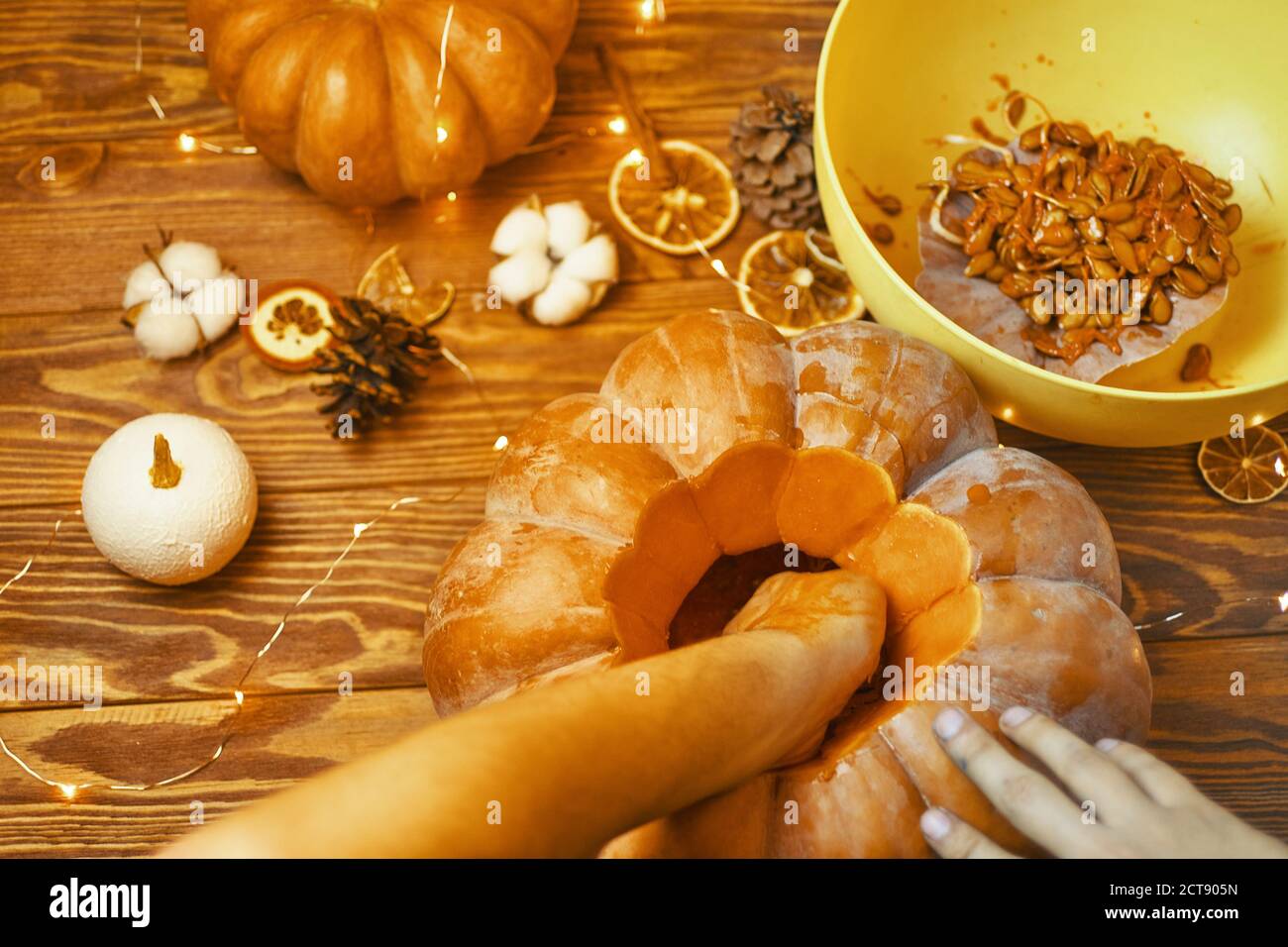 Festival d'autunno composizione con zucca. Il concetto di Halloween con facce intagliate sulla zucca. Una ciotola per semi di zucca e rifiuti. Garland, fette aranciate e coni di pino su fondo di legno. Foto Stock