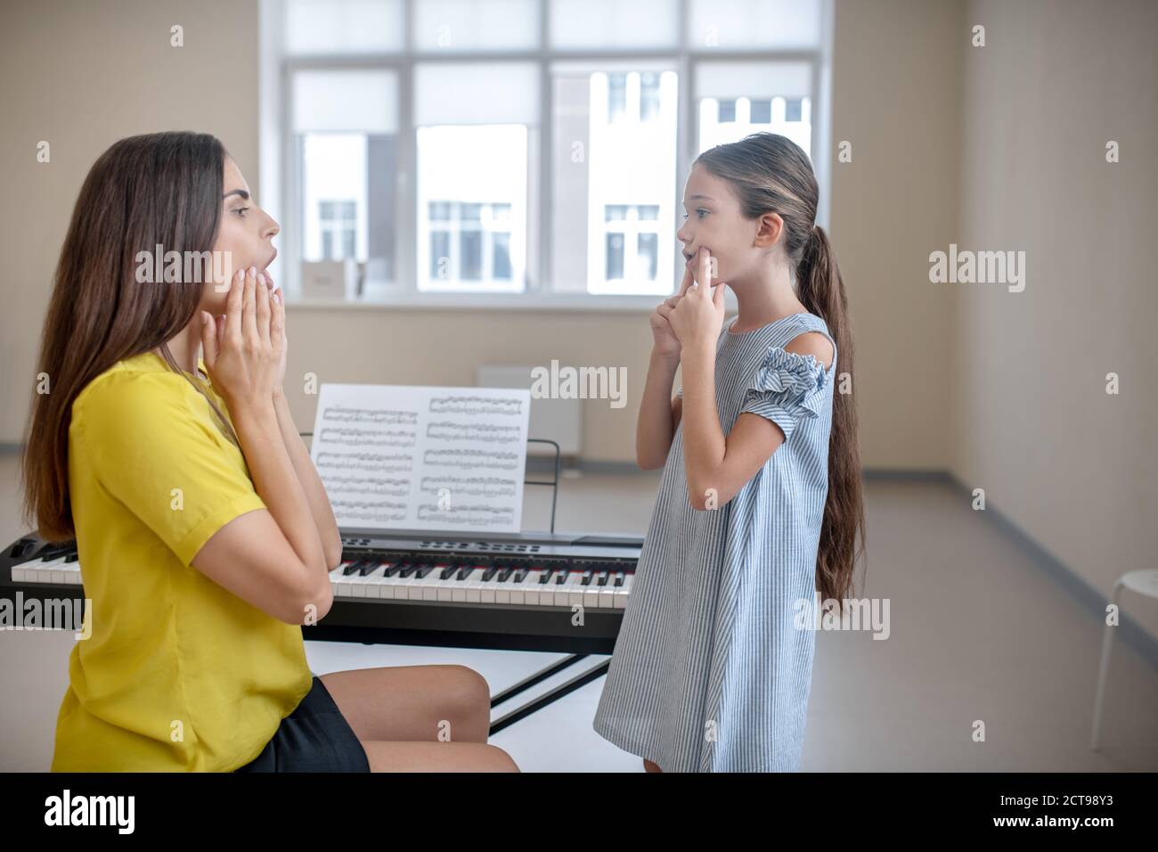 Ragazza in abito blu e il suo insegnante che fa esercizi di voce Foto Stock