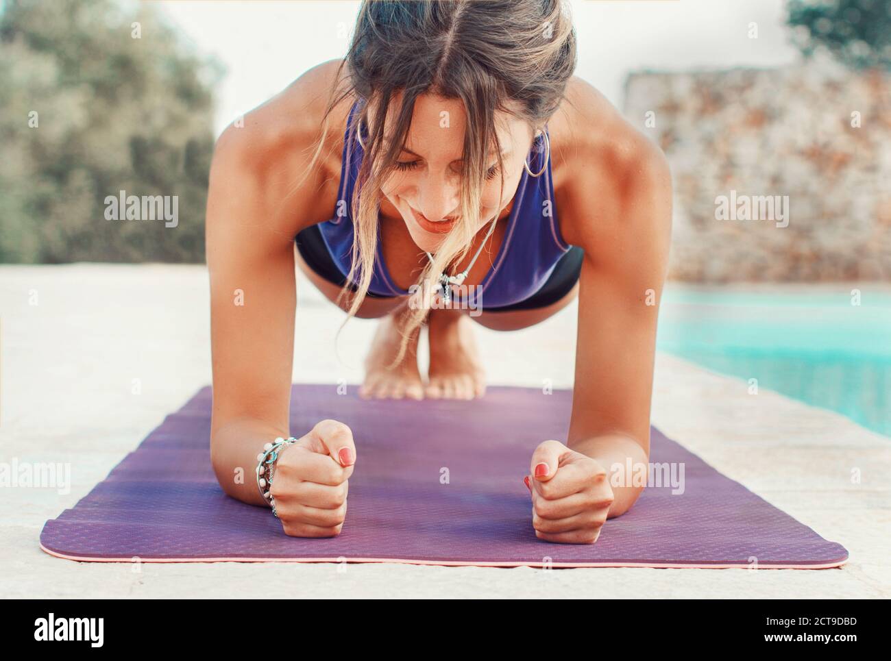 Giovane donna che pratica gomito tavola posa vicino a una piscina vicina su Foto Stock