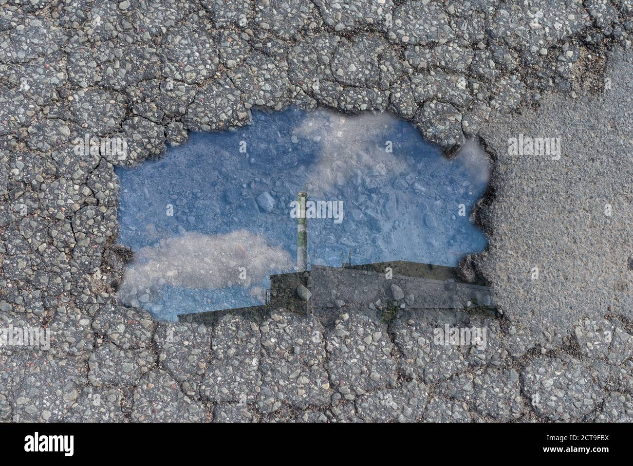 Una buca nel manto stradale. Un buco nel terreno.con silhouette di fabbrica e il camino con il fumo in un cielo blu.all'aperto. Foto Stock