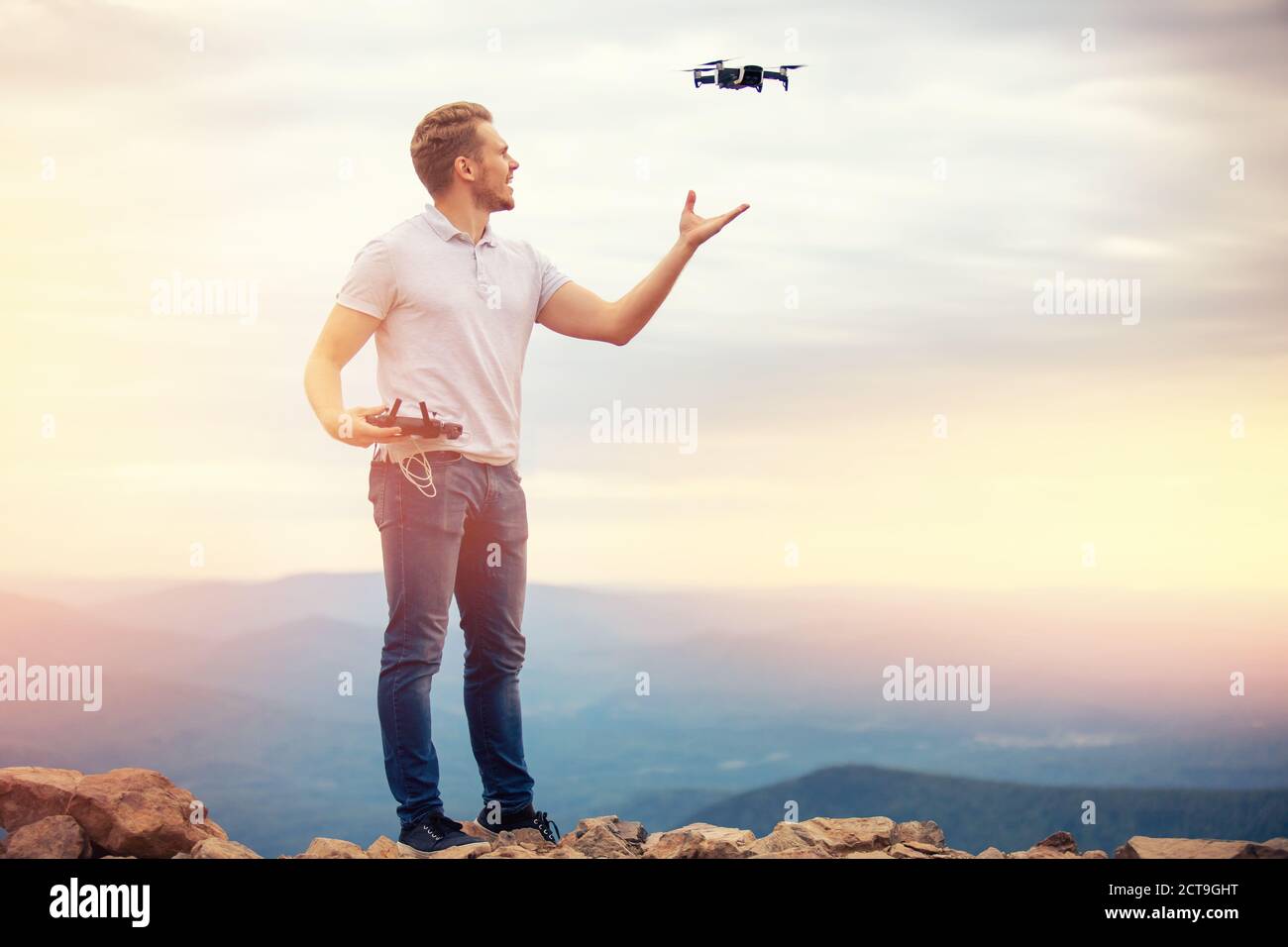 L'uomo felice controlla il drone, effettua l'atterraggio del quadcopter sulla mano, il tramonto Foto Stock