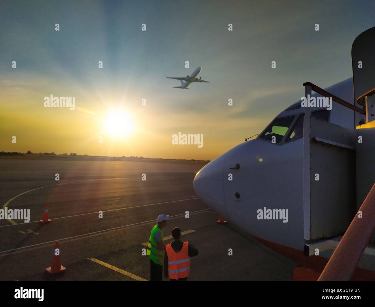 davanti a un aereo commerciale bianco che si erge sulla pista dell'aeroporto al tramonto. Foto Stock