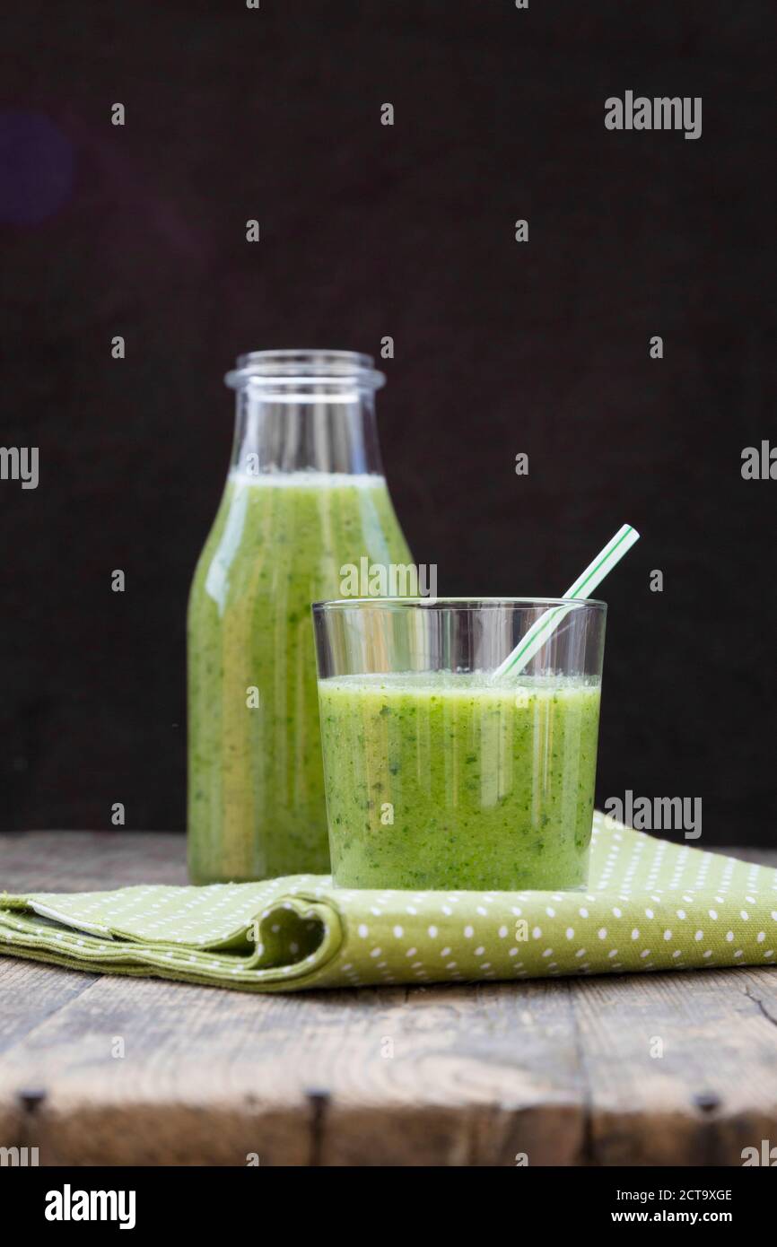Bottiglia di vetro e il vetro del frullato verde, fatta di spinaci, insalata di rucola, mela, arancio, banana e cetriolo, sul tavolo di legno Foto Stock