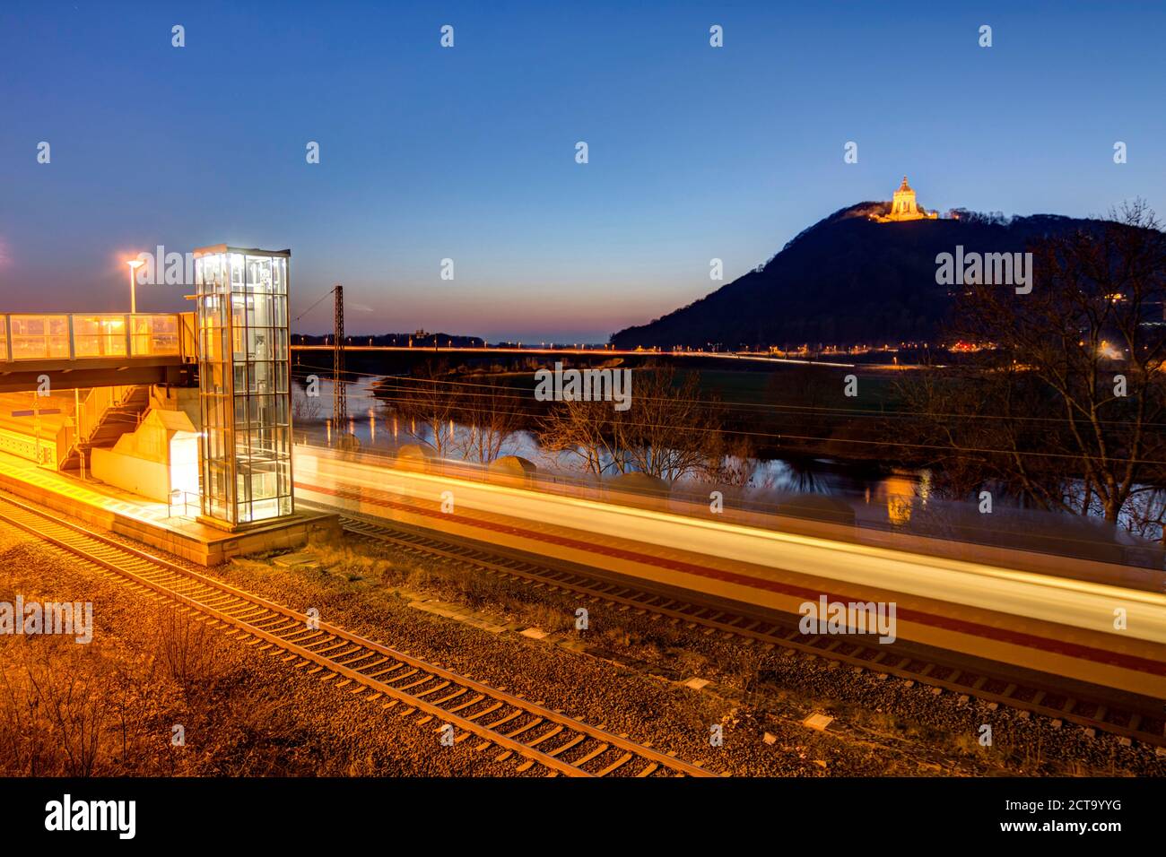 In Germania, in Renania settentrionale-Vestfalia, Porta Westfalica, illuminate Emperor-Wilhelm monumento di Wiehen colline con la piattaforma e i binari ferroviari nella parte anteriore Foto Stock