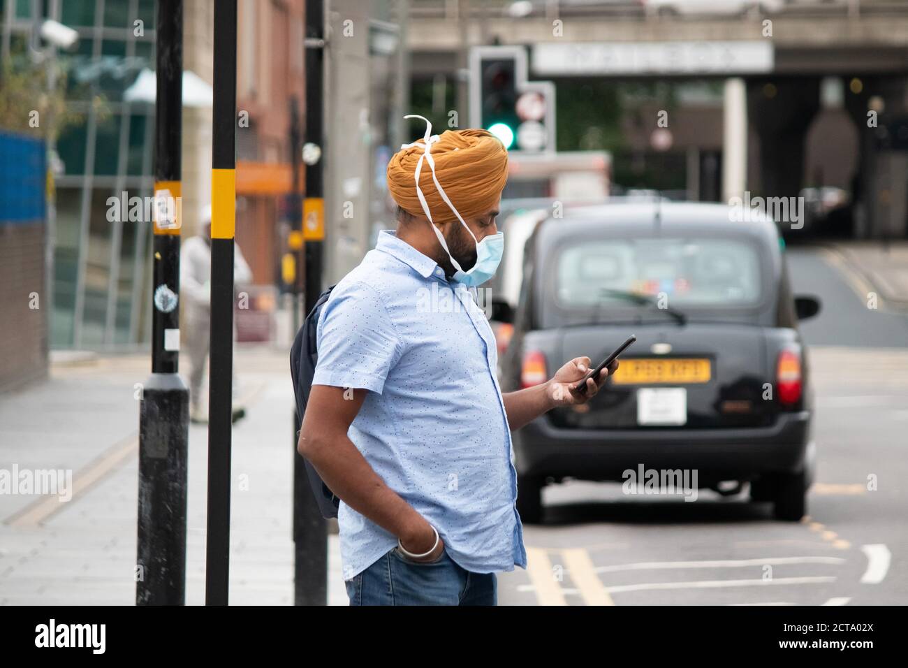 Immagine scattata il giorno in cui le restrizioni di Coronavirus sono state applicate a Birmingham. Nella foto, un uomo controlla il telefono mentre attende fuori dalla stazione ferroviaria di Birmingham in Navigation Street. Foto Stock