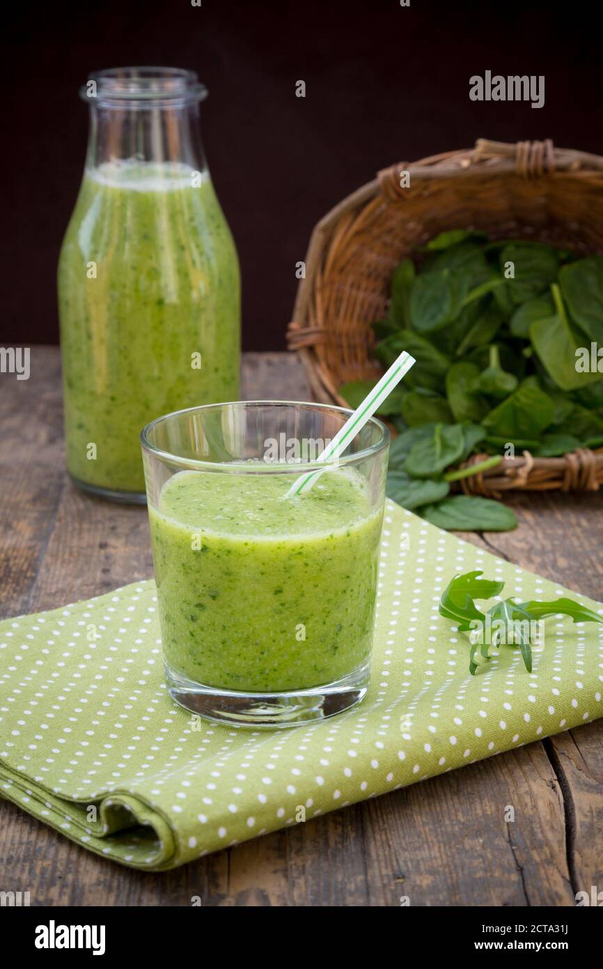 Bottiglia di vetro e bicchiere di frullato verde, fatto di spinaci, insalata di razzo, mela, arancia, banana e cetriolo, su tavola di legno di stoffa Foto Stock