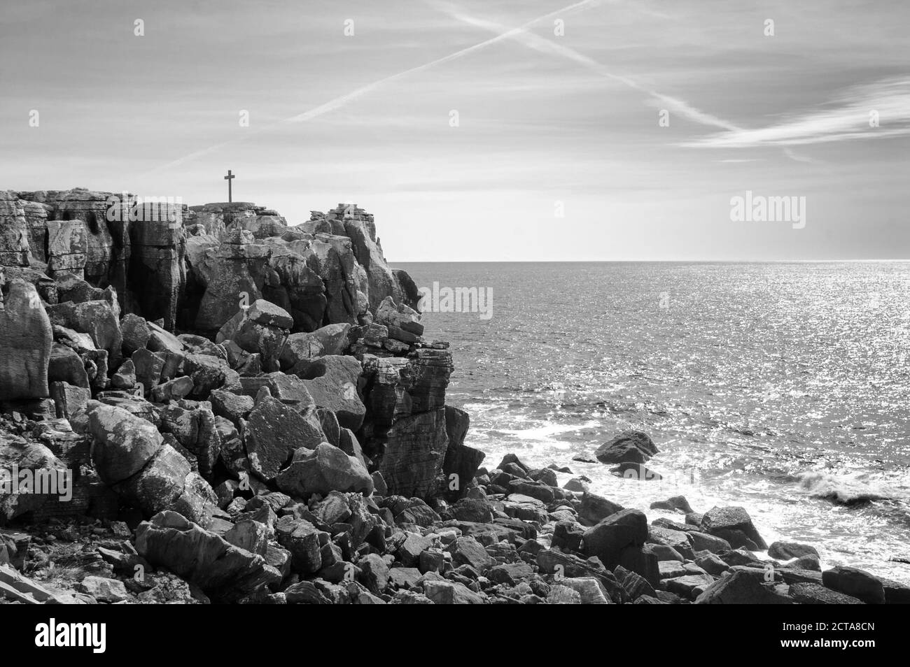 Attraversa la cima rocciosa sull'oceano. Croce nel cielo - traccia piano. Peniche, Portogallo. Foto obsolata. Bianco e nero. Foto Stock