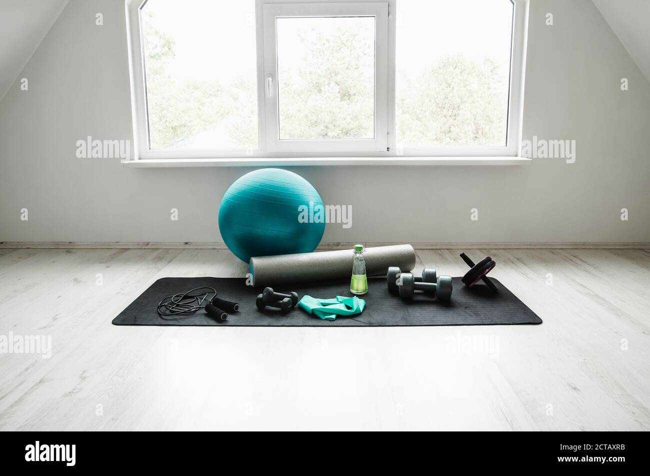 Camera vuota e luminosa, moderna e bianca, con accessori per l'allenamento a casa. Palla yoga, resistenza esercizio lattice fascia, rullo in schiuma, pesi, corda salto, wa Foto Stock