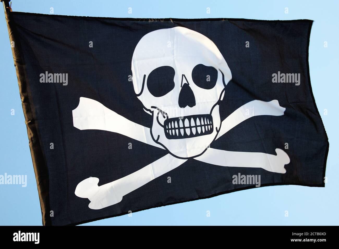 Jolly Roger scull e crossbones bandiera pirata battenti su un immagine fotografica blu trasparente Foto Stock