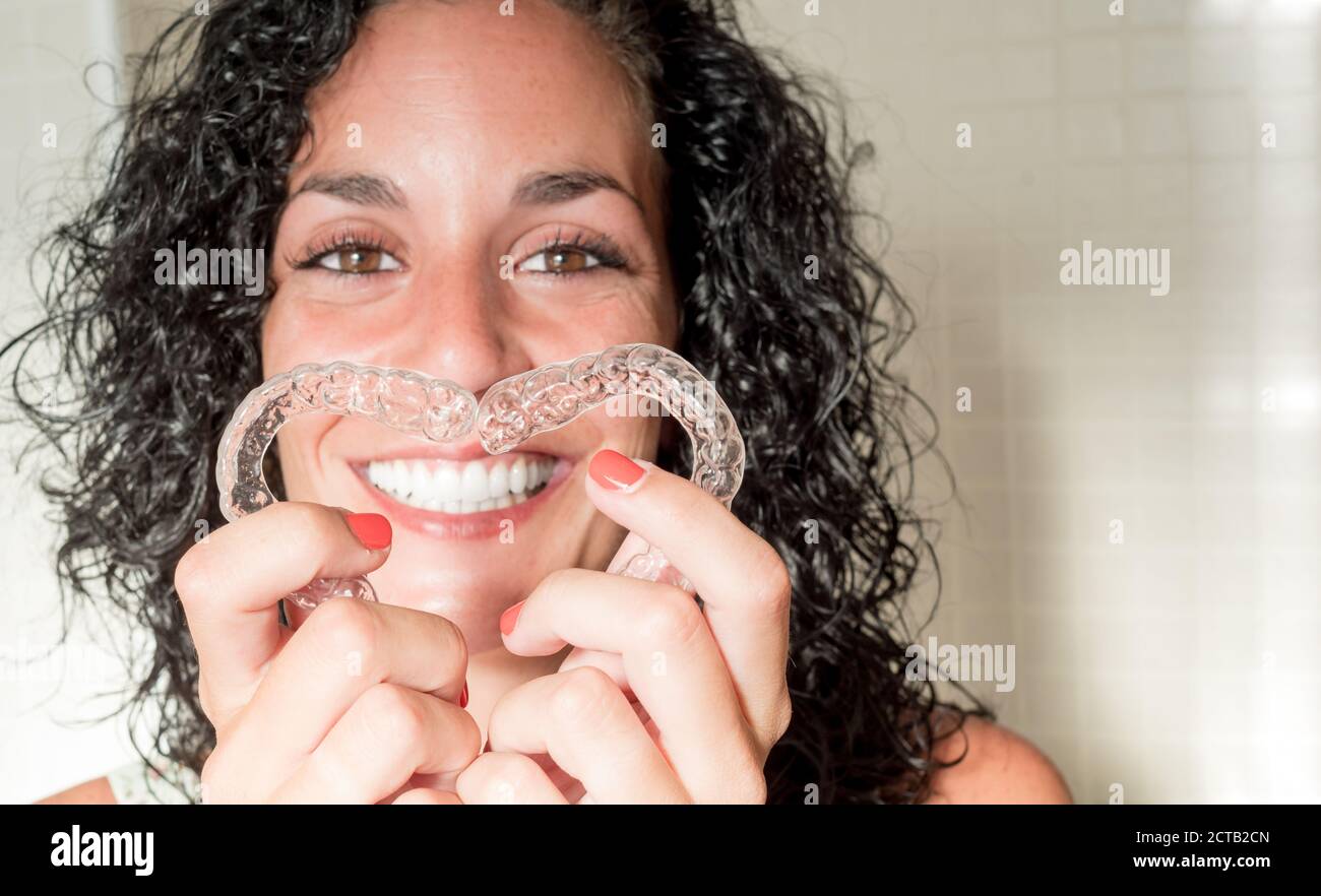 giovane donna sorridente che forma il cuore con i suoi allineatori invisibili in silicone per la correzione dentale. Trattamento dentale. Ortodonzia mobile. Foto Stock