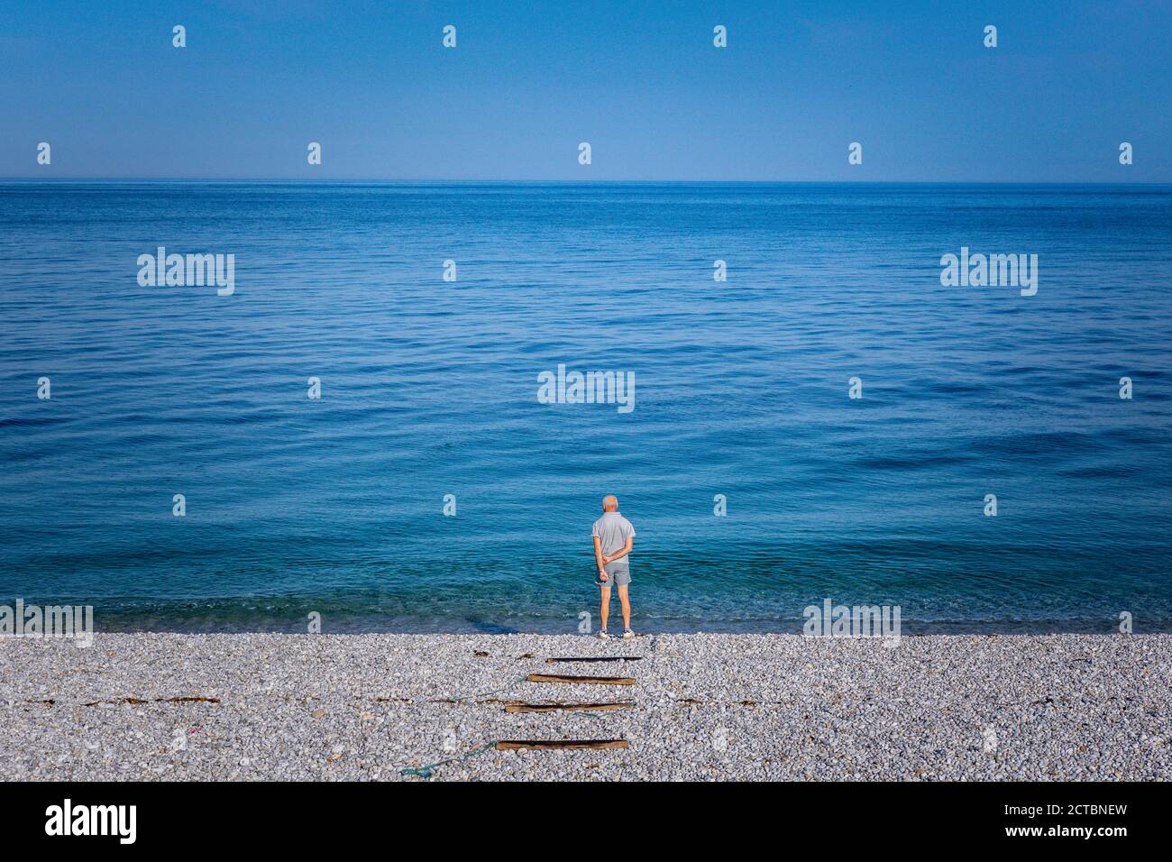 Uomo solitario sulla spiaggia che guarda all'orizzonte Foto Stock