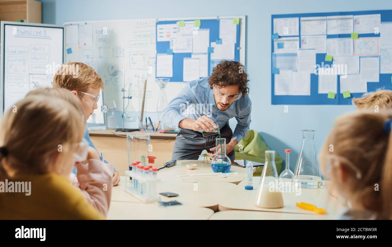 Scuola elementare di chimica Classroom: Insegnante entusiasta insegna Gruppo di bambini, mostra esperimenti scientifici mescolando sostanze chimiche nel becher Foto Stock