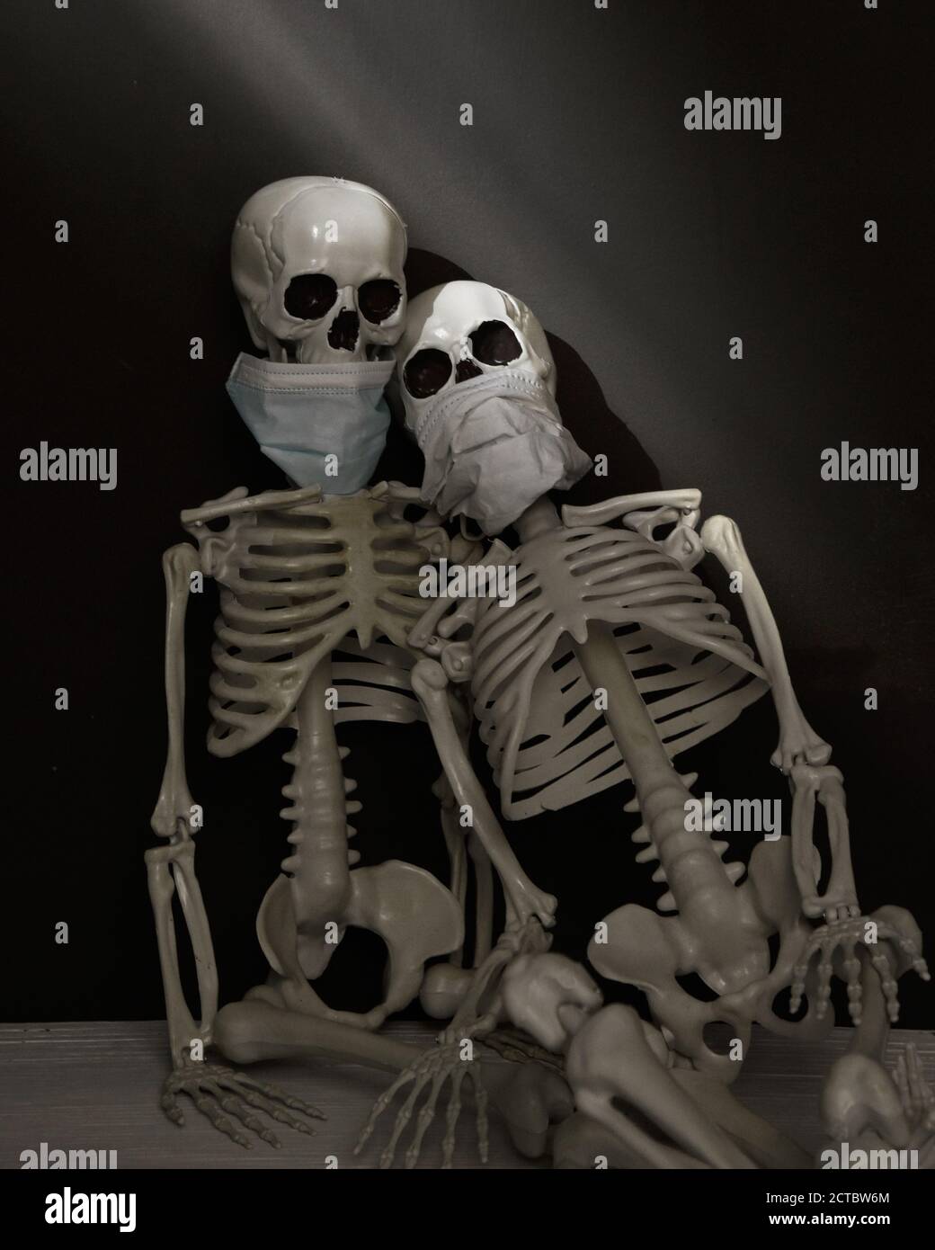 Due scheletri indossano maschere facila contro una parete nera con luce solare per un concetto spaventoso e strano decorazione halloween. Foto Stock