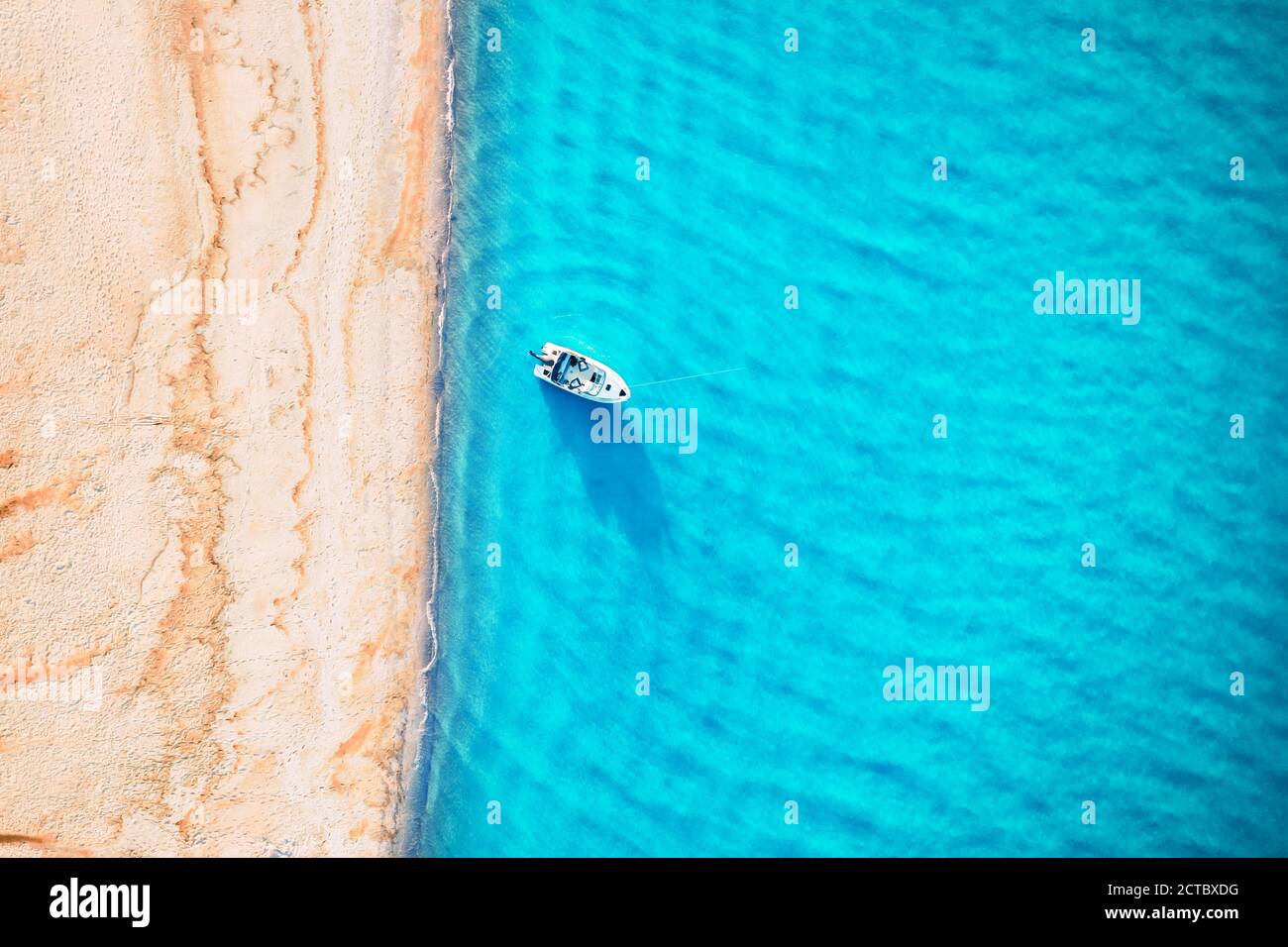 Yacht bianco e onde turchesi dall'alto. Spiaggia con sabbia gialla illuminata dalla luce del sole. Viaggi estate vacanze stagcape sfondo da drone Foto Stock