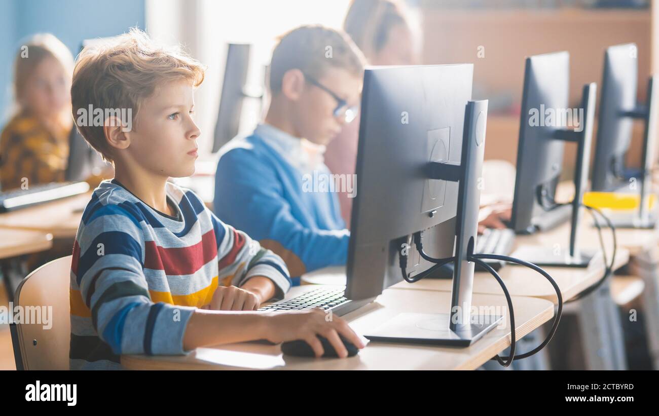 Scuola elementare Scienza Aula: Piccoli studenti intelligenti seduti in fila e lavorare su Personal computer, imparare linguaggio di programmazione per Foto Stock