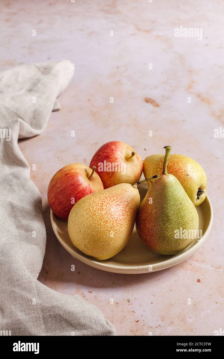 Mele e pere di stagione in un piccolo piatto su uno sfondo di marmo rosa con un tovagliolo di lino beige. Foto Stock