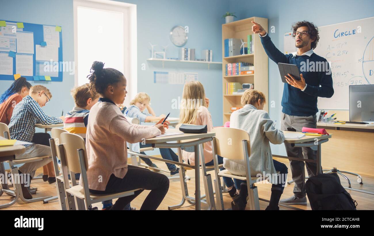 Insegnante entusiasta che dà una lezione in scuola elementare a classe piena di bambini diversi. Gruppo di bambini multietnici intelligenti che imparano nuove cose Foto Stock