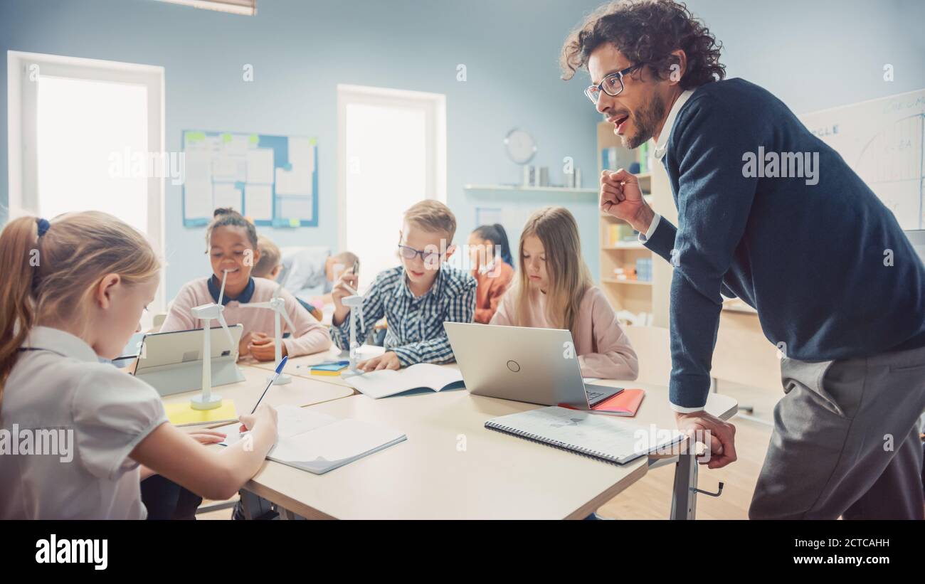 Nella scuola elementare: Classe di giovani bambini intelligenti lavorano come un team che utilizza i computer tablet per programmare le turbine eoliche. In aula con i bambini che imparano Foto Stock