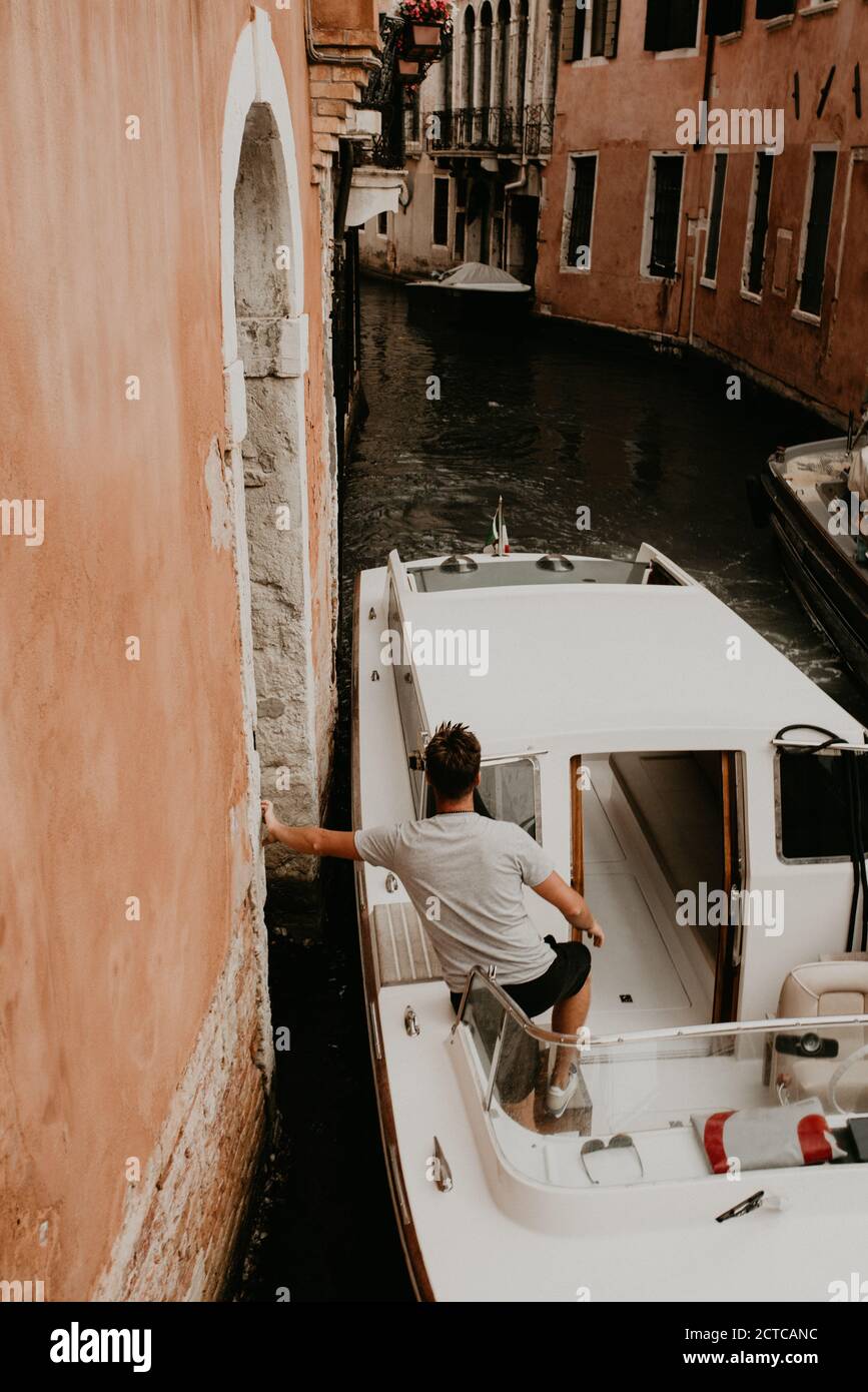 Un uomo in una T-shirt bianca si trova in una barca e appoggia la mano sul muro. Gondolieri barche a vela. Foto Stock