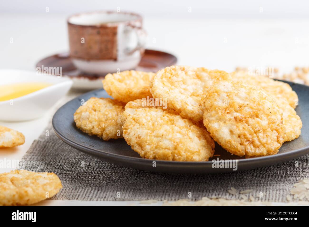Biscotti tradizionali giapponesi di patatine di riso con salsa di miele e soia su un piatto di ceramica blu e una tazza di caffè su uno sfondo di legno bianco. Vista laterale, Foto Stock