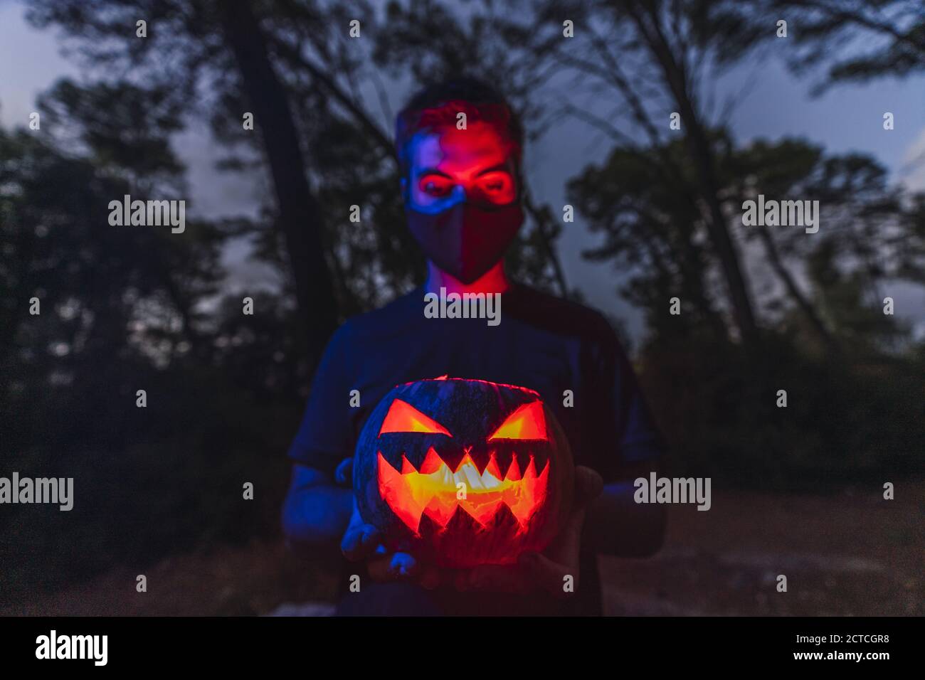 Giovane maschio che indossa una maschera nera e tiene un Halloween zucca con una faccia spaventosa Foto Stock