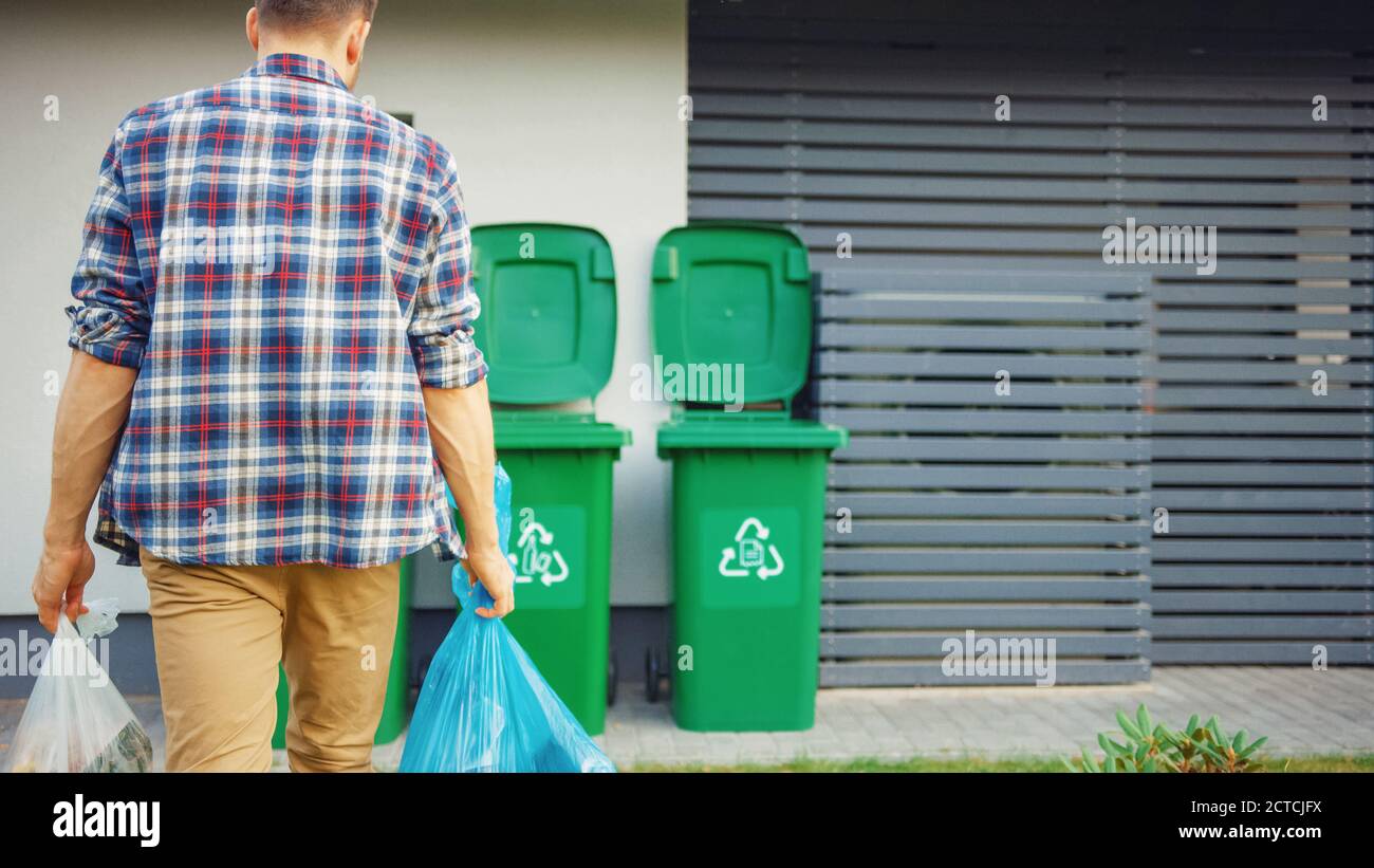 L'uomo caucasico sta camminando fuori della sua casa per estrarre due sacchetti di plastica del cestino. Un sacchetto per rifiuti viene smistato con rifiuti di alimenti biologici, altro Foto Stock