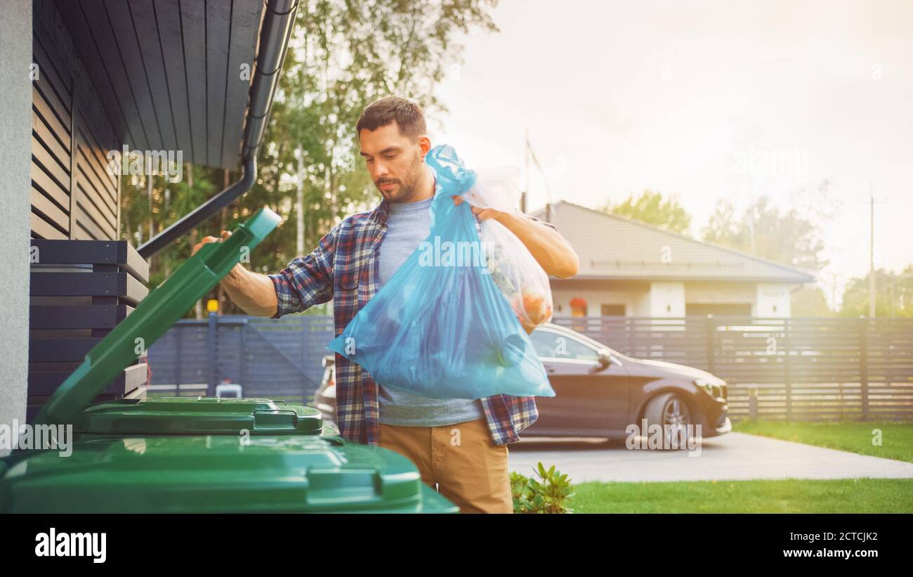 L'uomo caucasico sta gettando via due sacchetti di plastica del cestino vicino alla sua casa. Un sacchetto di immondizia è smistato con spreco biologico di alimento, altro con Foto Stock