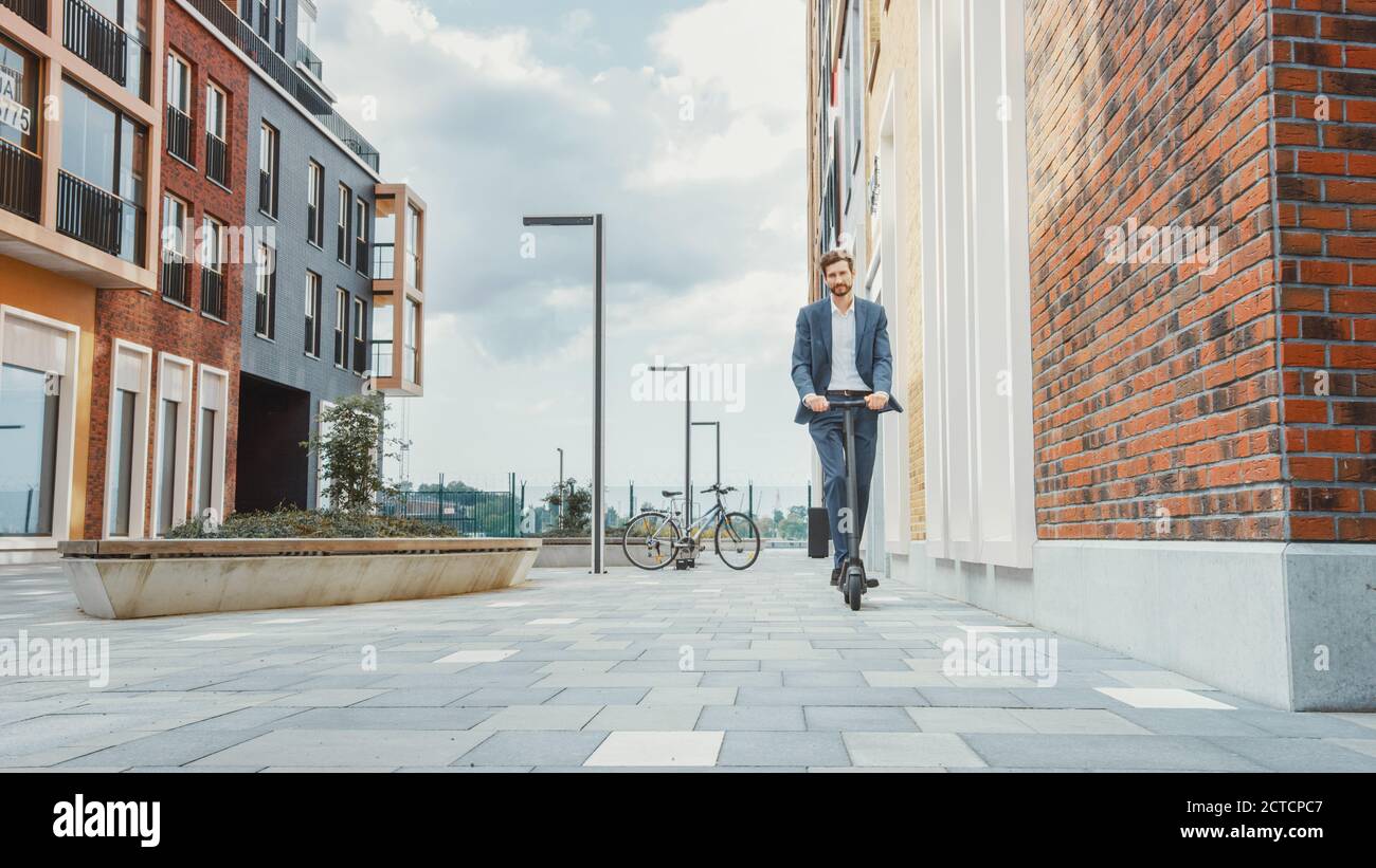 Giovane uomo d'affari in una tuta Equitazione per lavorare su uno scooter elettrico. L'imprenditore moderno usa il trasporto ecologico contemporaneo per andare in un ufficio Foto Stock