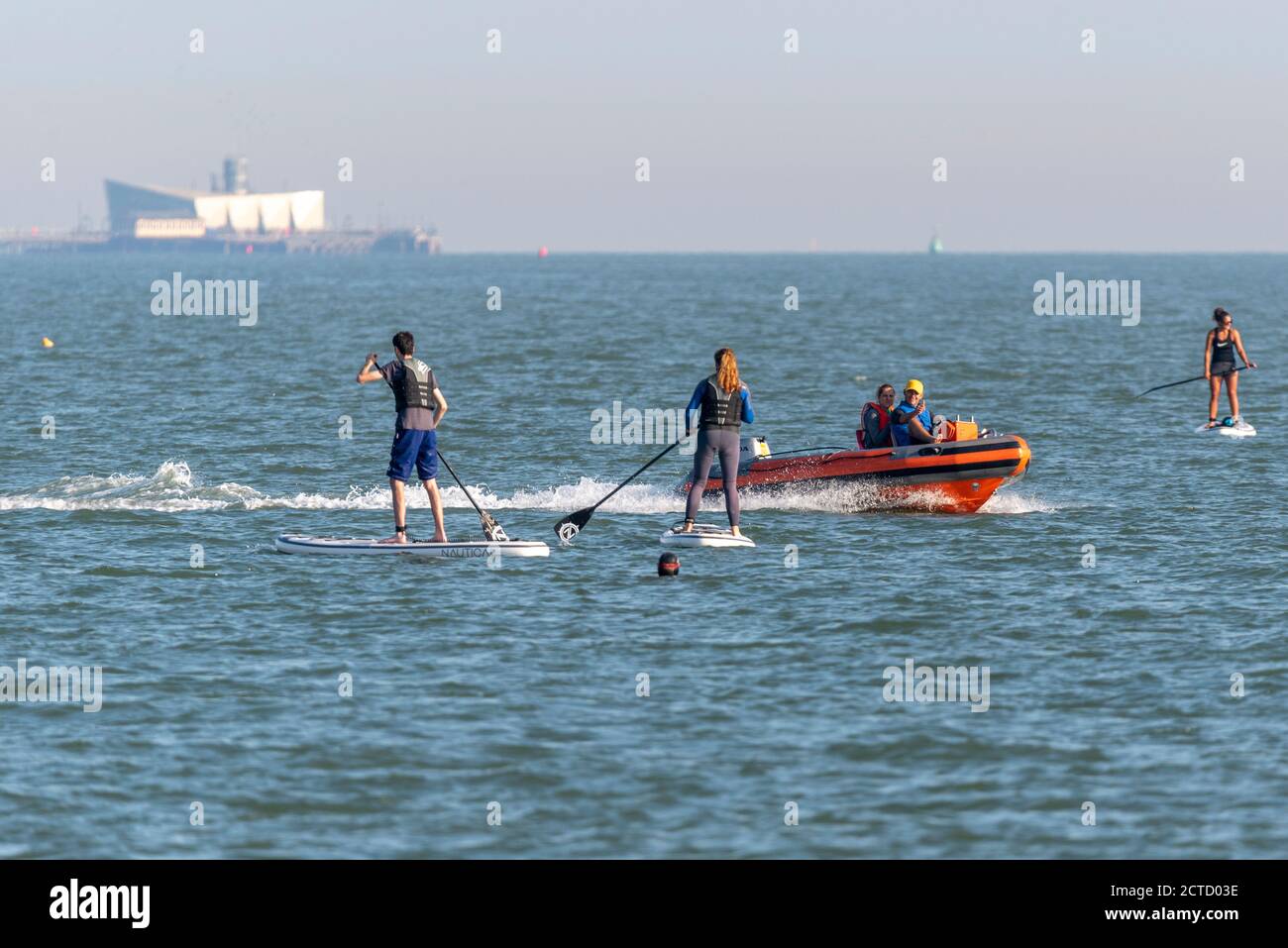 Controllo delle imbarcazioni di sicurezza sui paddle boarders al largo di Southend on Sea, Essex, Regno Unito. Sport acquatici nell'estuario del Tamigi. Sport acquatici in mare con dinghy motore Foto Stock
