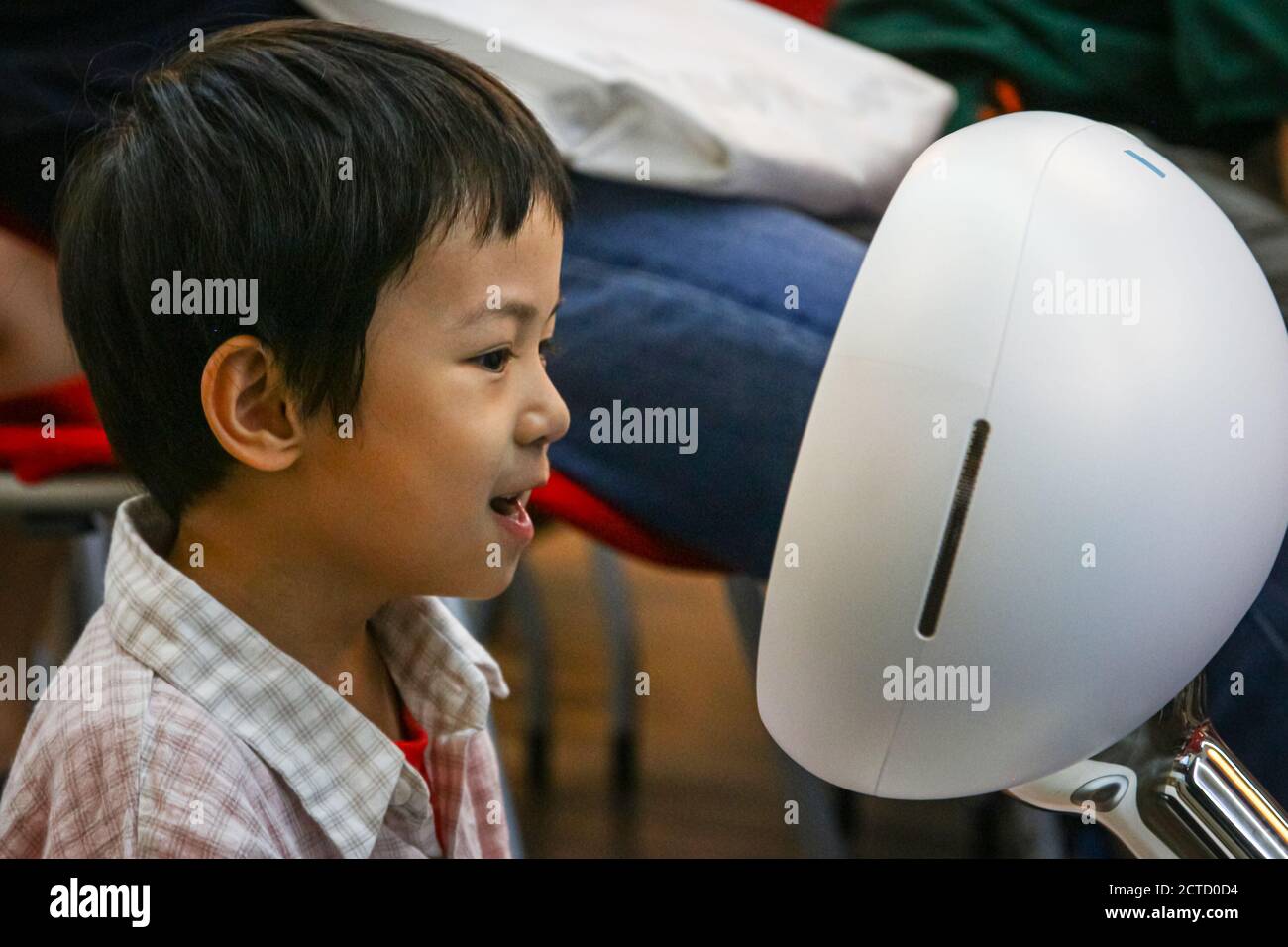 Un ragazzo che parla felicemente con un robot, desideroso di ricevere una risposta. Foto Stock