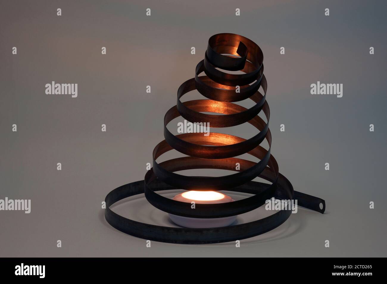 Primo piano di una spirale di un vecchio orologio. L'oggetto è un po' arrugginito a causa dell'età. Molla a spirale. È illuminato da una luce di colore arancione. Foto Stock