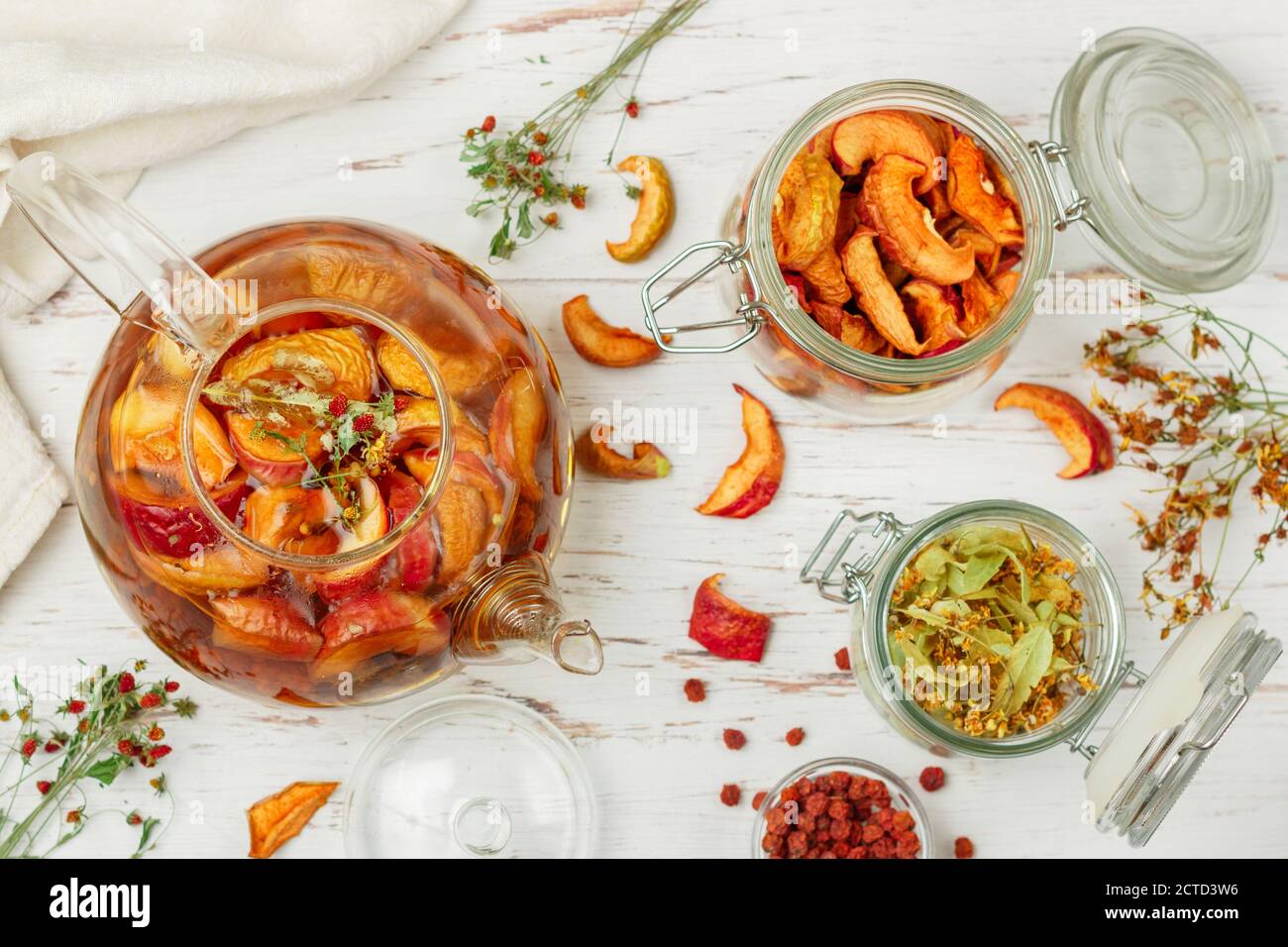 Tisane vitaminiche. Deliziosa e sana bevanda calda autunnale a base di mele secche, Linden, Rowan, fragole selvatiche in una teiera di vetro su un tavolo bianco Foto Stock