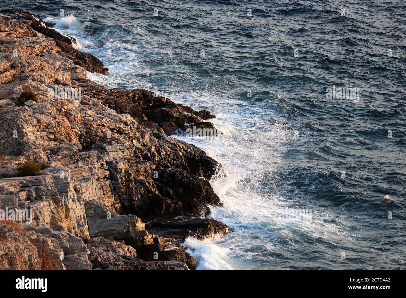 Le onde si infrangono sulle rocce sul mare con spruzzi bianchi. Acqua blu schiumosa su una pietra, sfondo mare Foto Stock