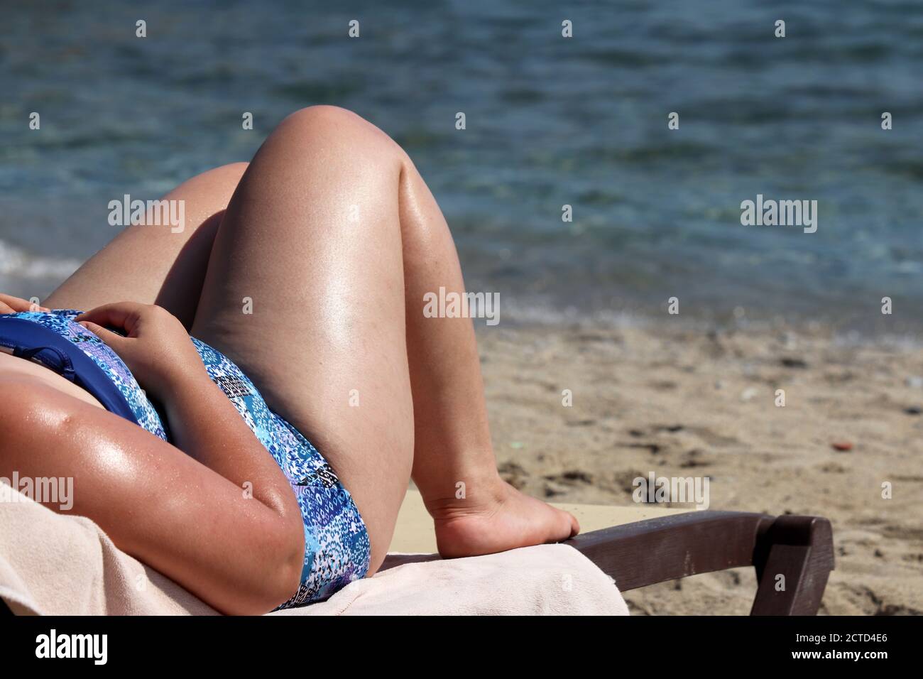 Donna grassa abbronzarsi su una spiaggia su sfondo mare onde. Sovrappeso e concetto di obesità Foto Stock