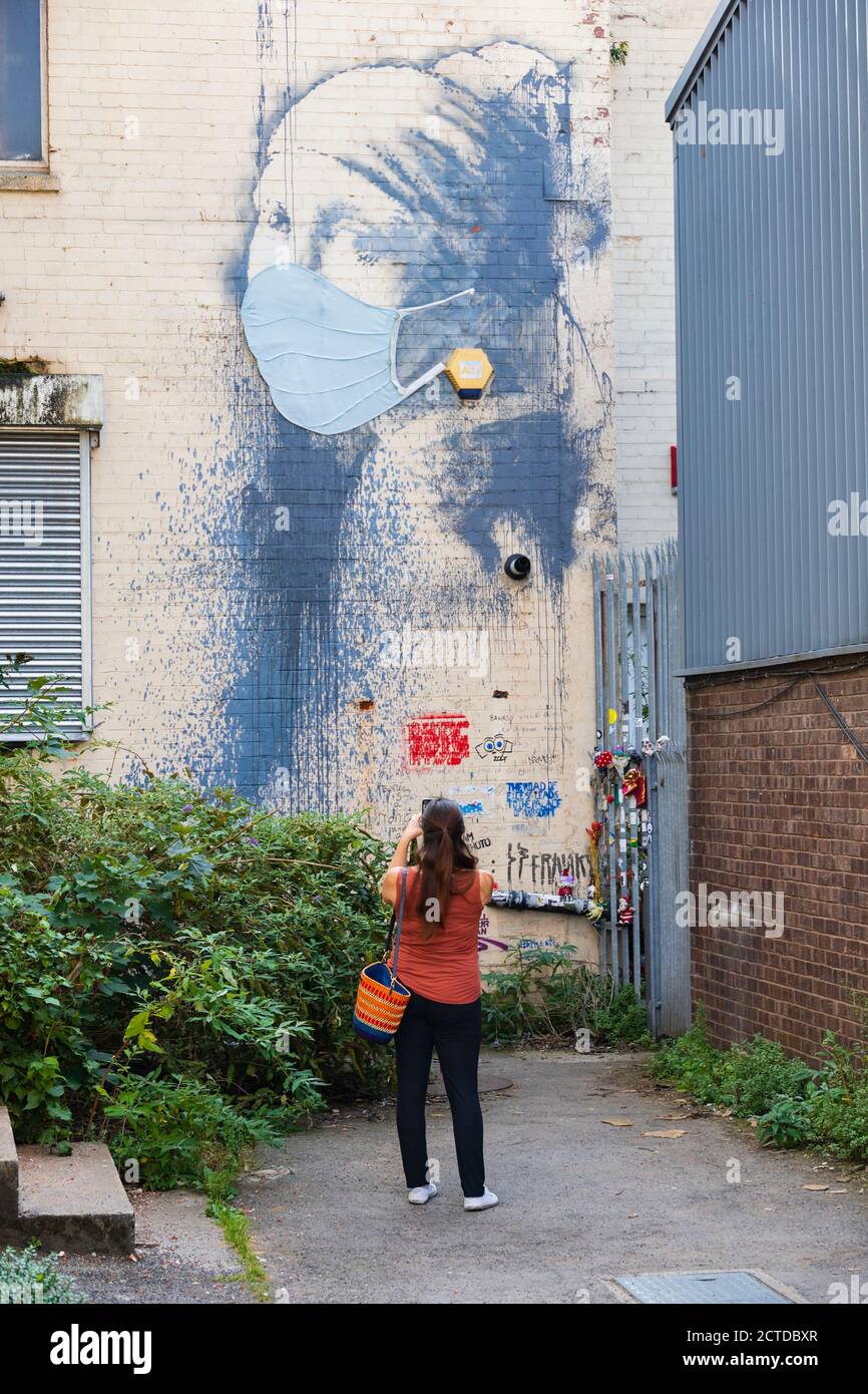 Donna turistica scatta una foto della Street art di Banksy "ragazza con il timpano trafitto". Ha una maschera facciale durante la pandemia di Covid 19. Bristol, Eng Foto Stock