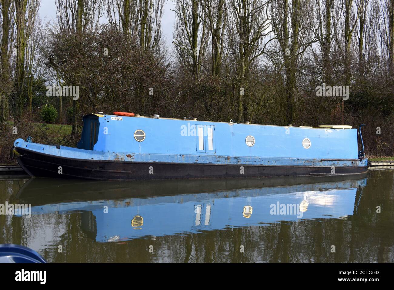 In questa foto scattata lungo il canale Grand Union nel Buckinghamshire, si riflette una barca blu che si trova in acque fisse Foto Stock