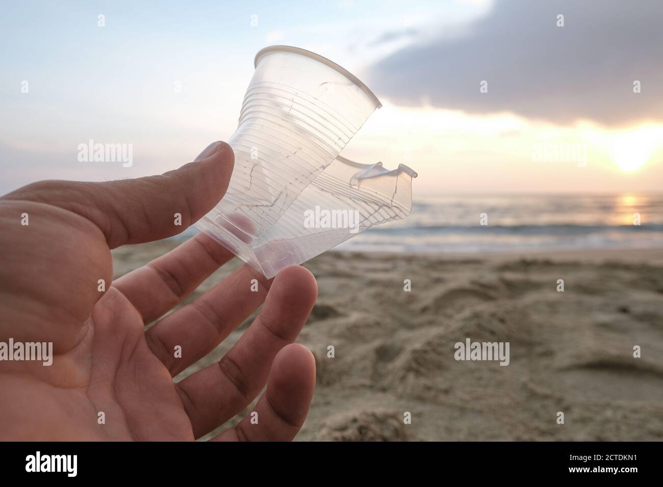 Man mano closeup con vetro di plastica isposable gettato su sabbia mare costa,inquinamento Foto Stock